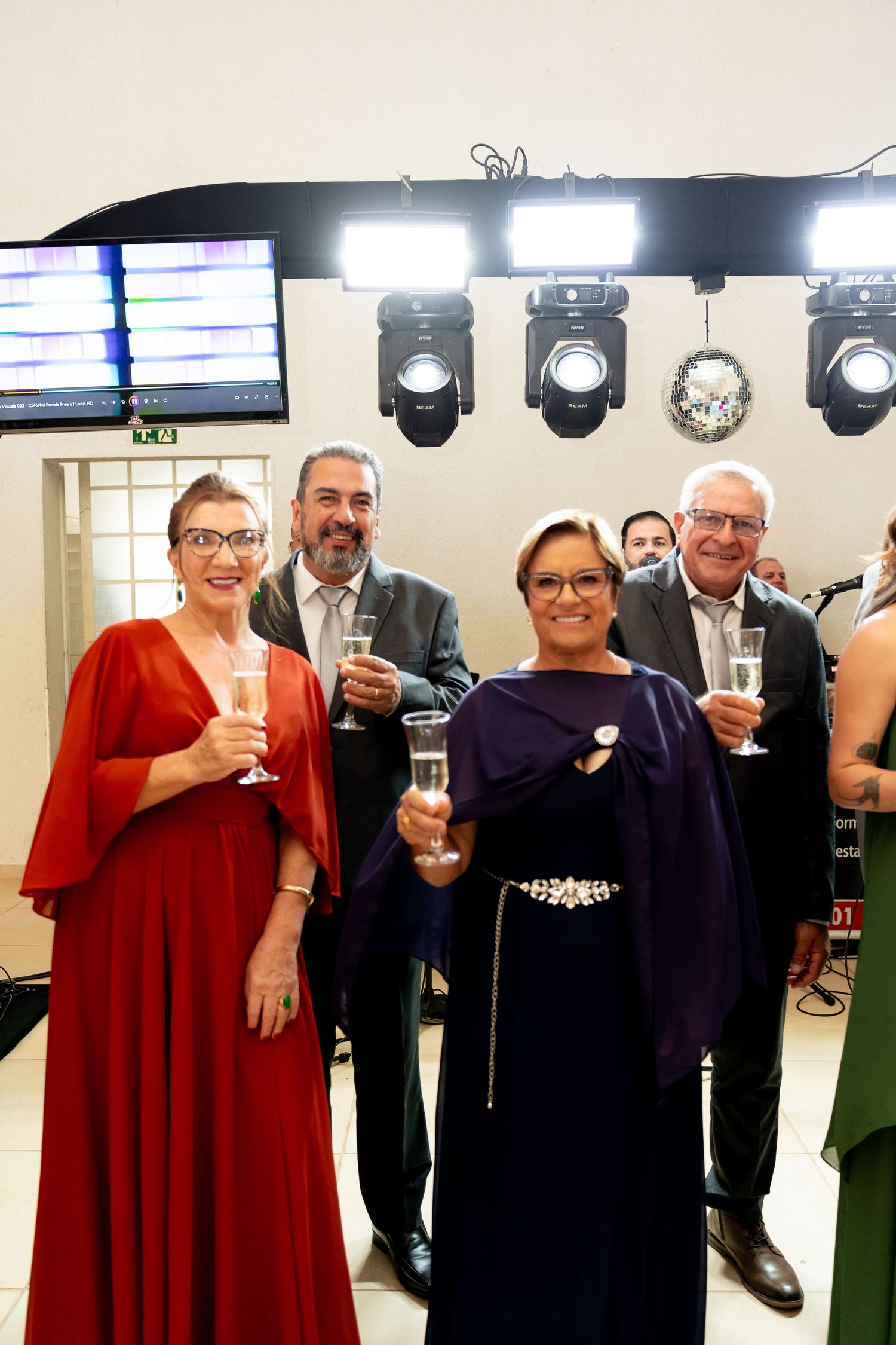 Elegantly dressed guests toasting with champagne glasses at a formal event under bright stage lights.