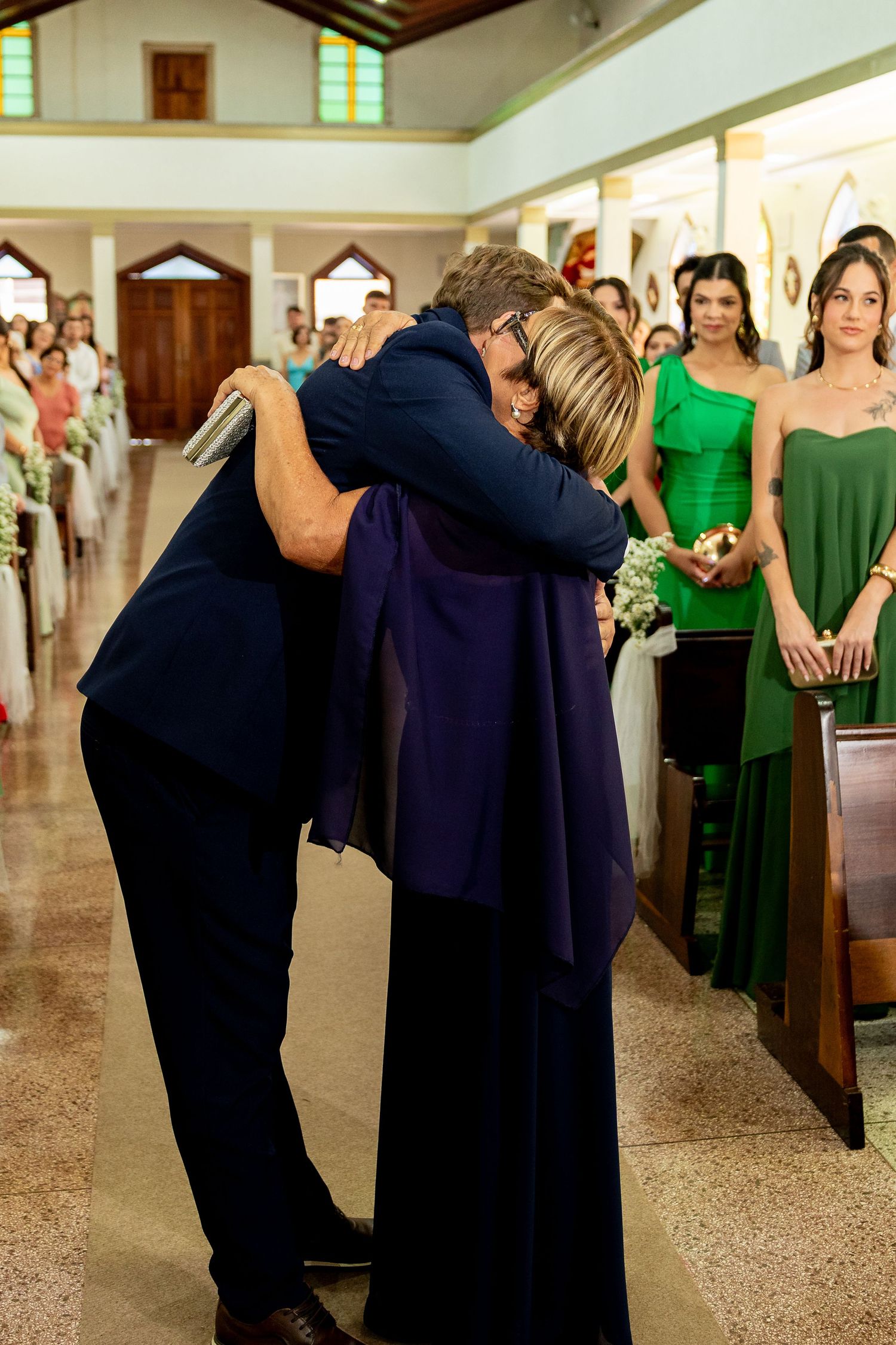 Emotional embrace between man in navy suit and woman in purple dress during wedding ceremony in church aisle.