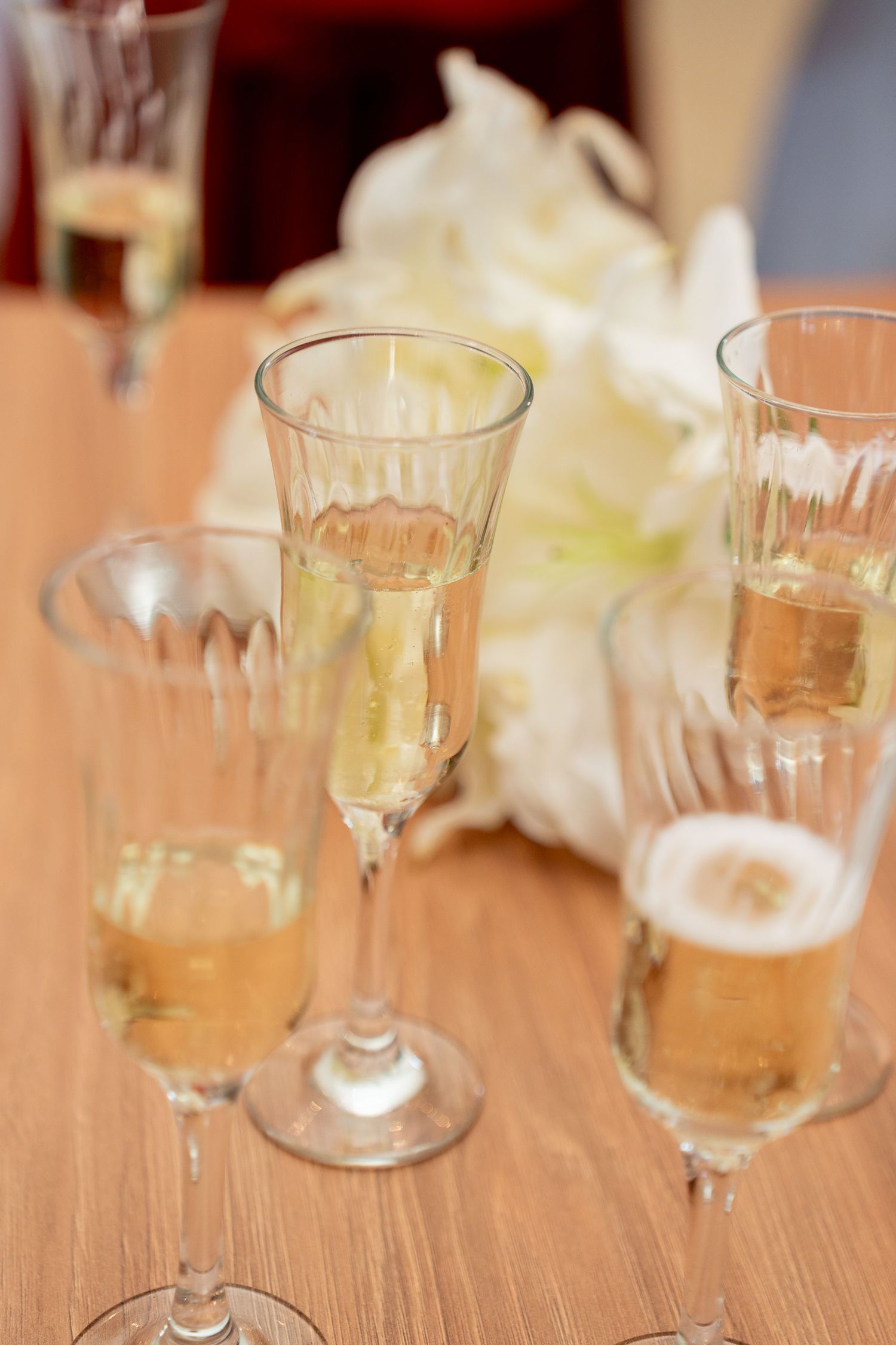 Elegant champagne flutes and beer glasses filled with golden beverages on a wooden table with white flowers.