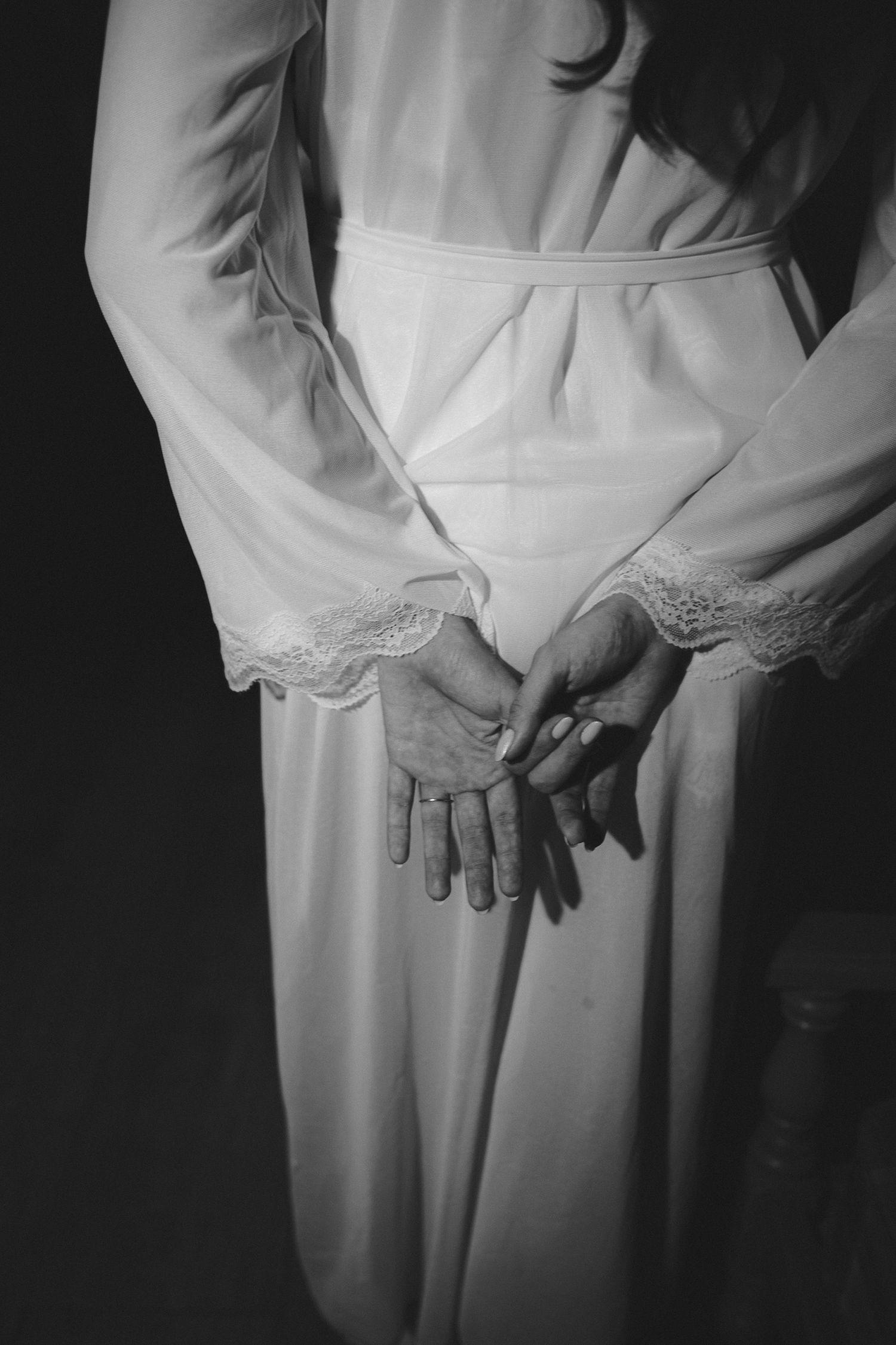 Black and white photo of a woman in a white lace-trimmed robe with hands clasped behind her back.