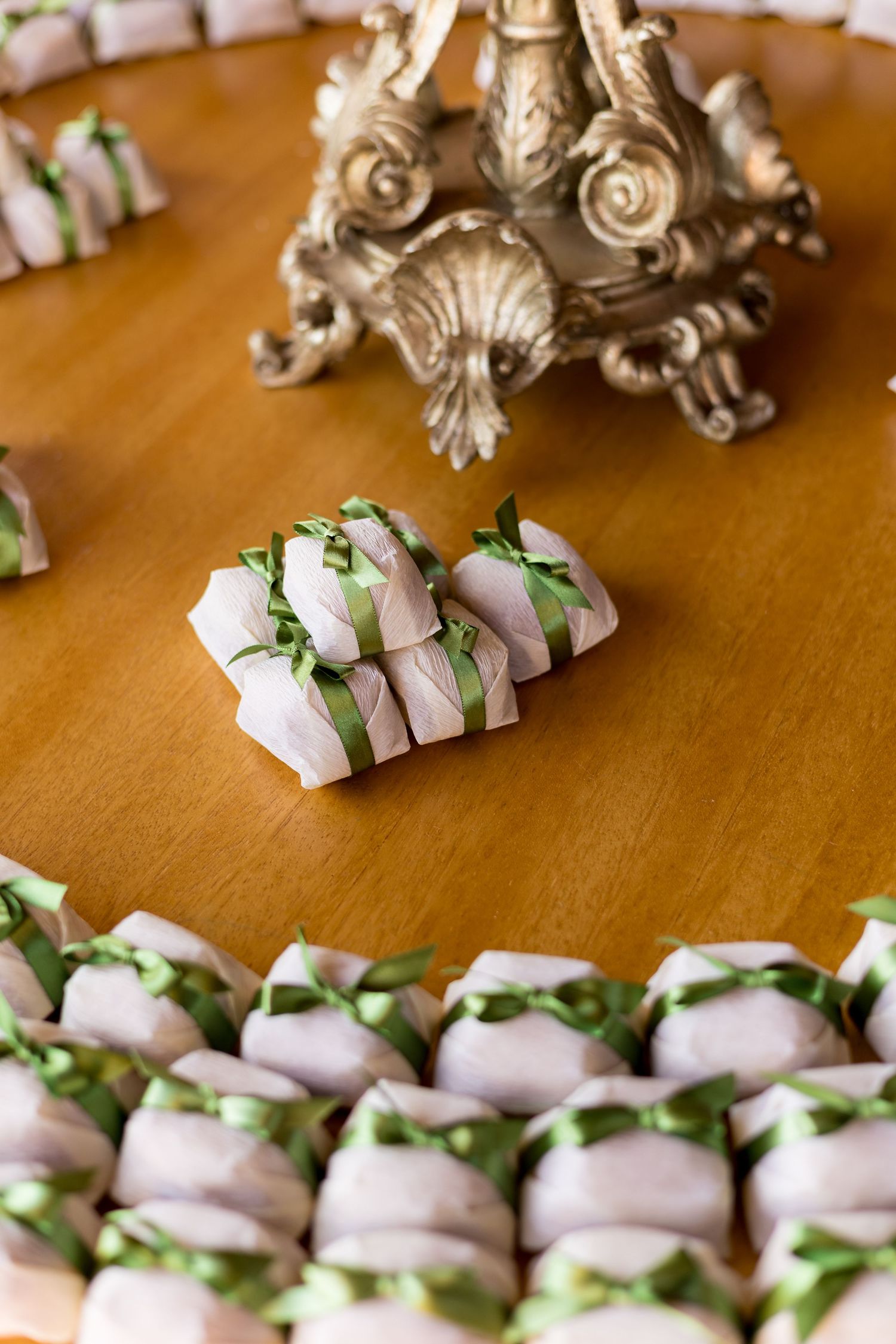 Small white gift boxes tied with green ribbons arranged on a wooden table around an ornate silver centerpiece.