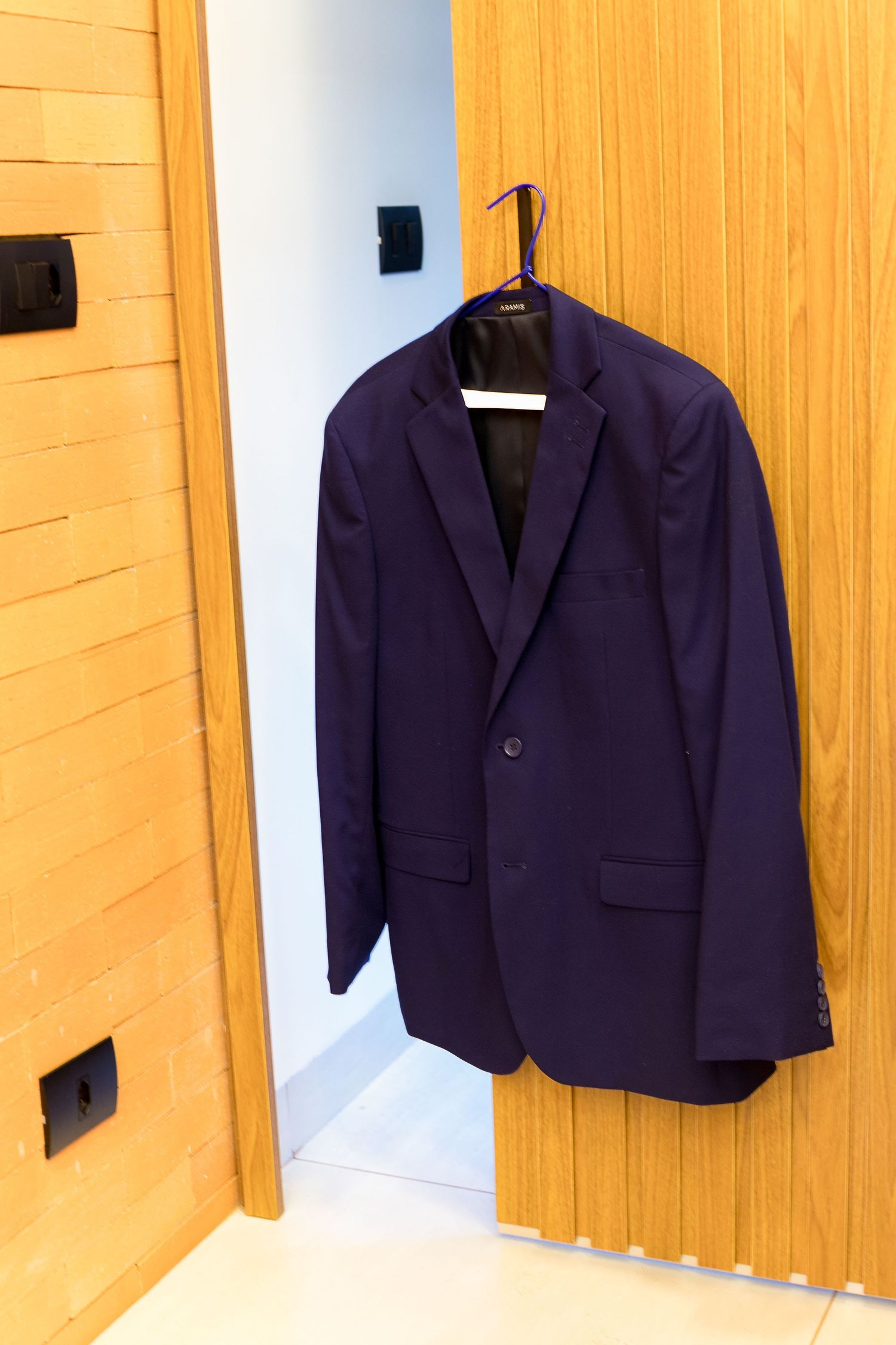 A navy blue men's blazer hanging on a wooden door hanger in a modern room.