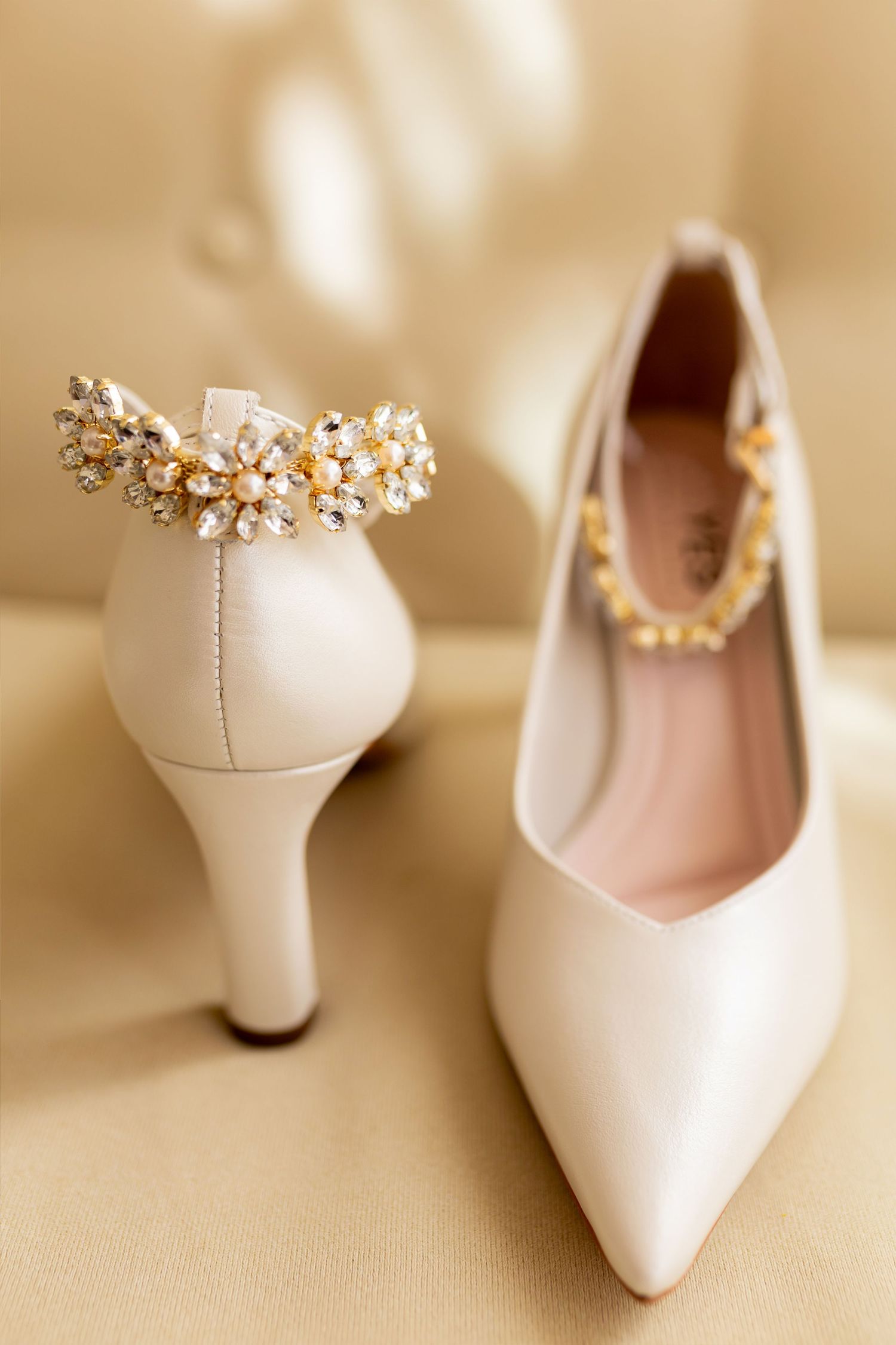 Elegant ivory bridal heels with crystal and pearl embellishments on gold satin background.