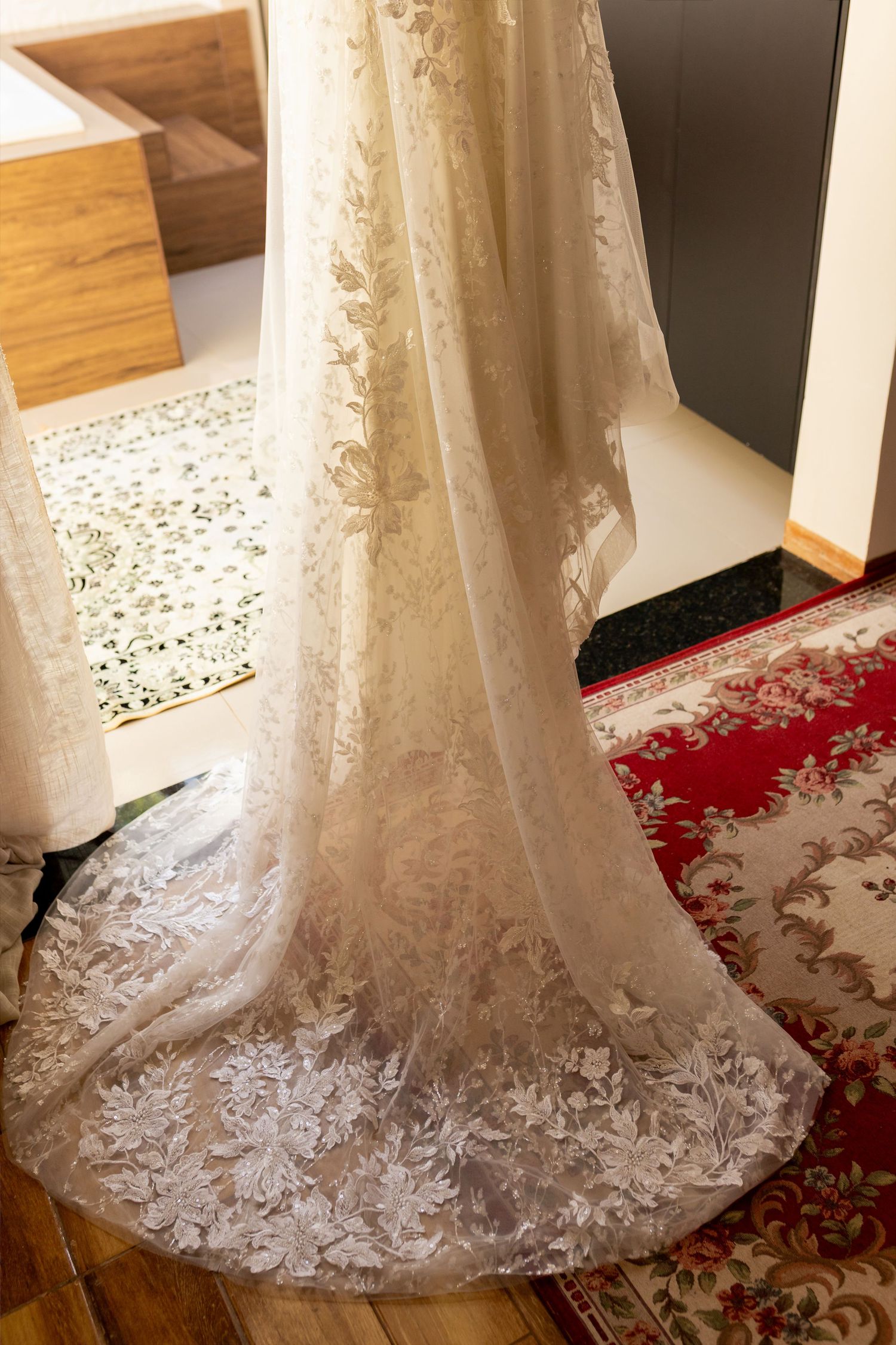 Elegant white lace wedding dress with floral embroidery displayed hanging in a room with hardwood floors.