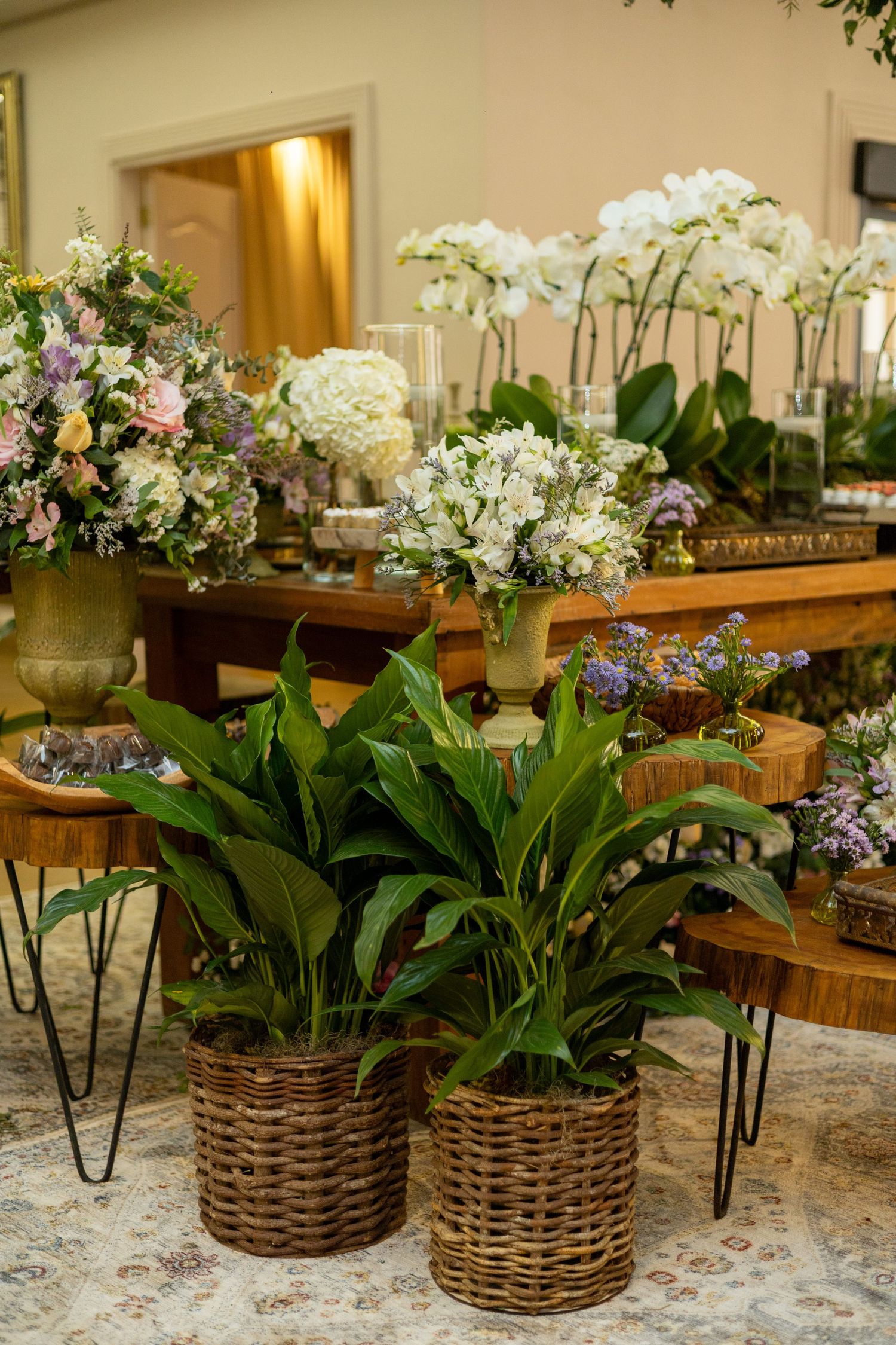 Elegant floral arrangement display with wicker baskets, white orchids, and mixed blooms on wooden tables at an event.