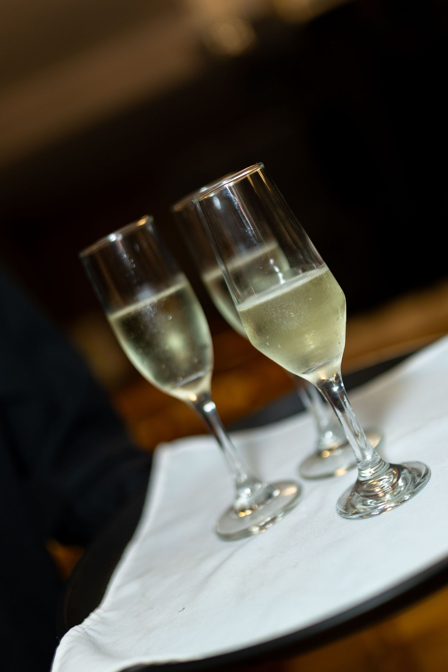 Two elegant champagne flute glasses filled with sparkling wine served on a white cloth tray.