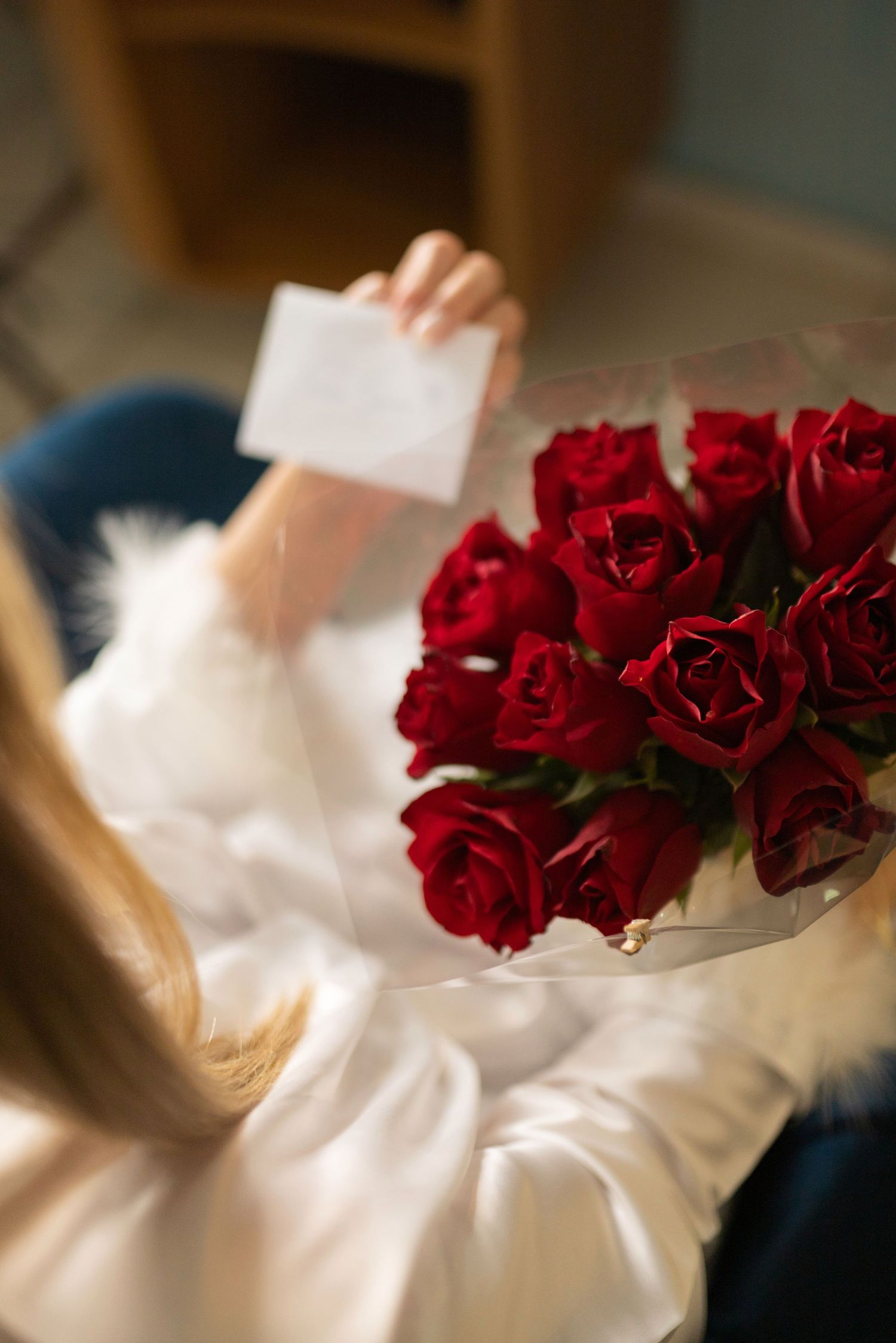 Woman in white blouse reading a card from a bouquet of red roses on Valentine's Day.