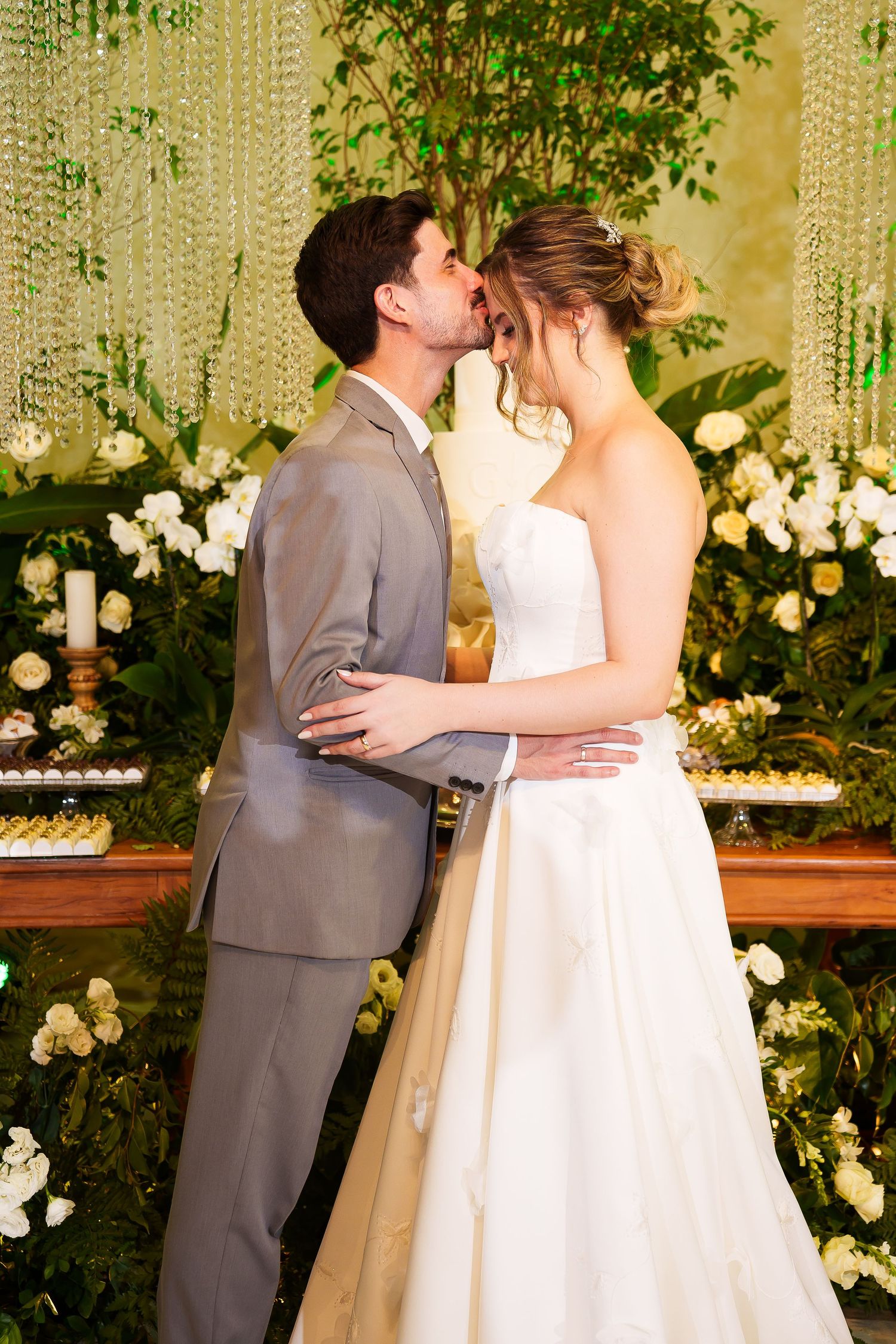 Bride and groom sharing a romantic kiss at wedding reception with white floral decorations and greenery backdrop.