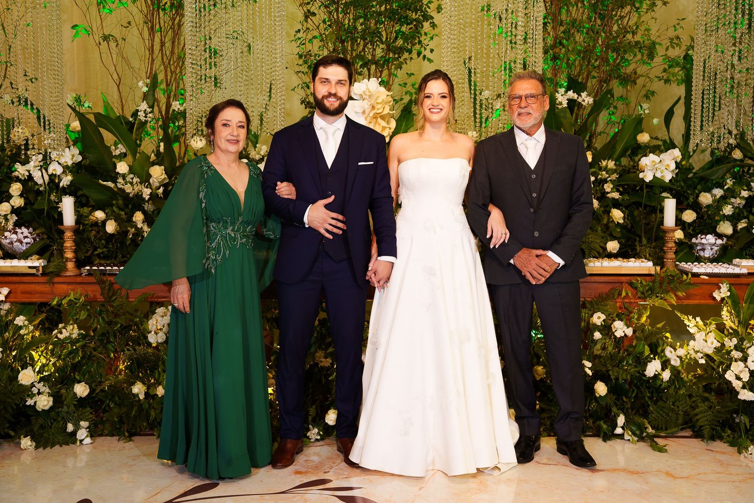 Bride and groom pose with family members at elegant wedding reception with floral backdrop.