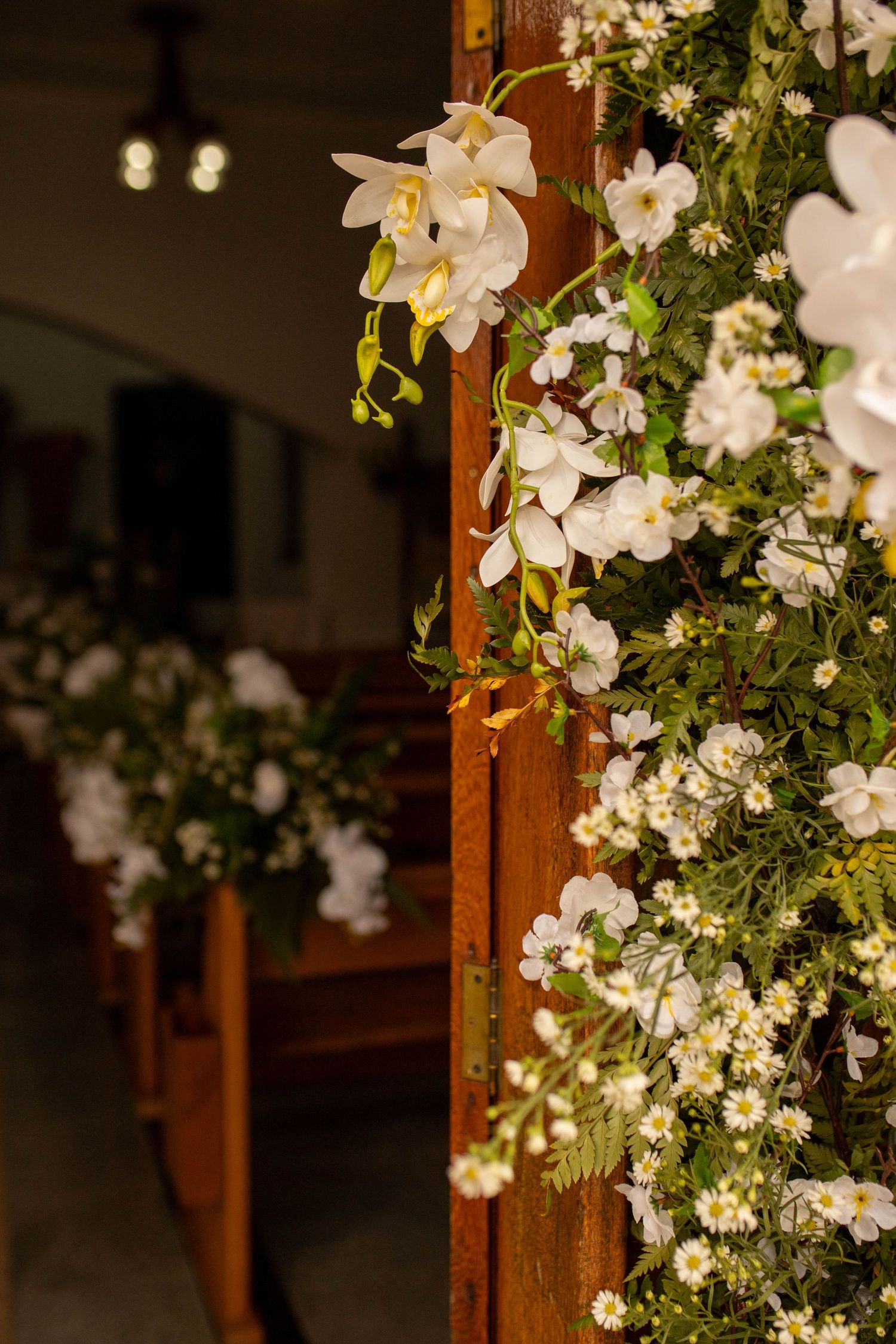 White flowers and greenery decorating a wooden church entrance with pews visible in the background.