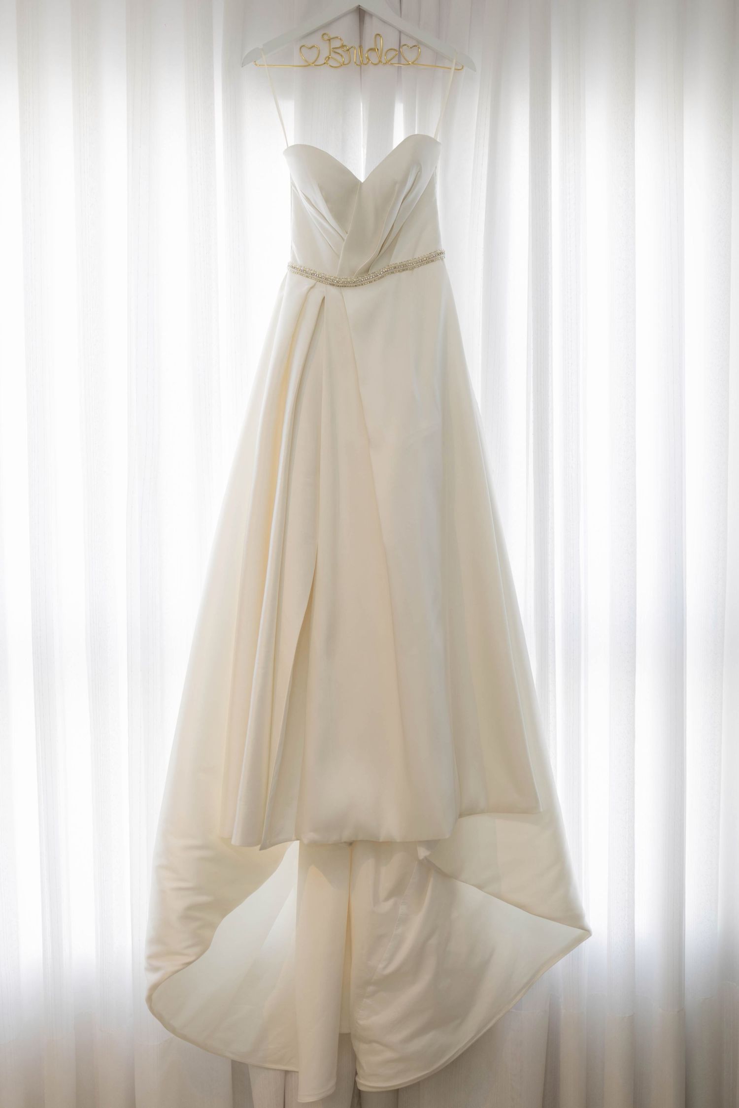 Elegant ivory strapless wedding gown with sweetheart neckline and high-low skirt hanging on a decorative hanger.