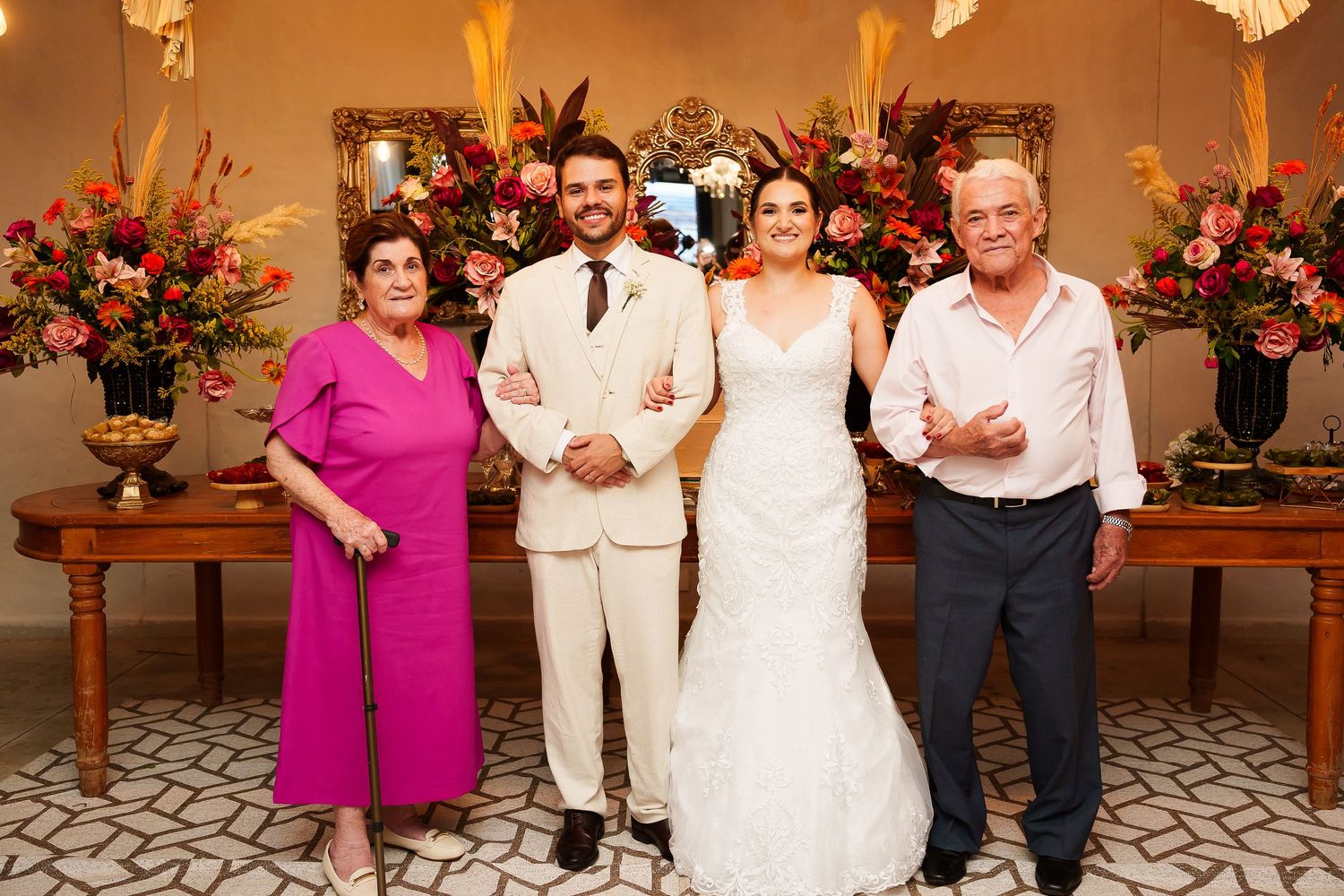 Bride and groom pose with family members in front of floral arrangements at an elegant wedding reception venue.