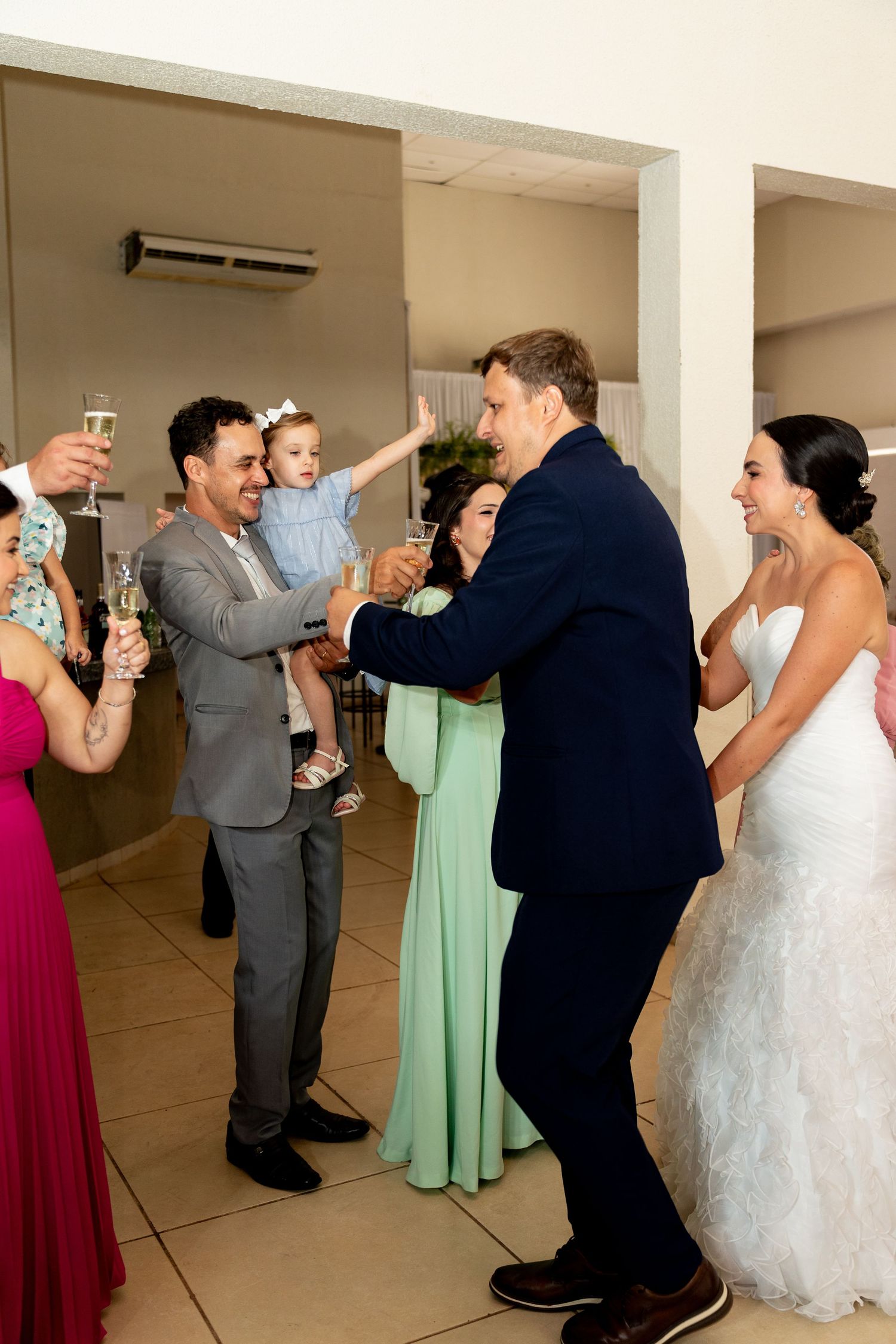 Bride and groom celebrate with wedding guests, toasting with champagne while a man holds a toddler at the reception.