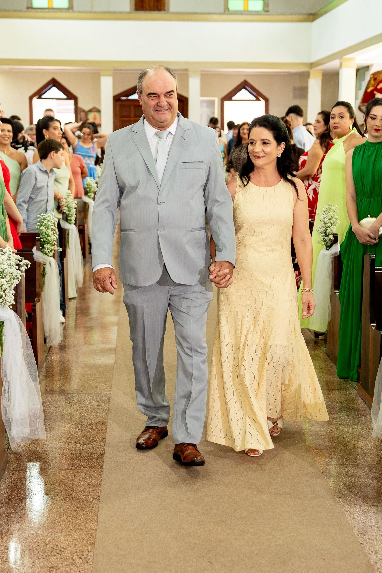 Couple walking down church aisle during wedding ceremony, man in gray suit, woman in elegant yellow gown.