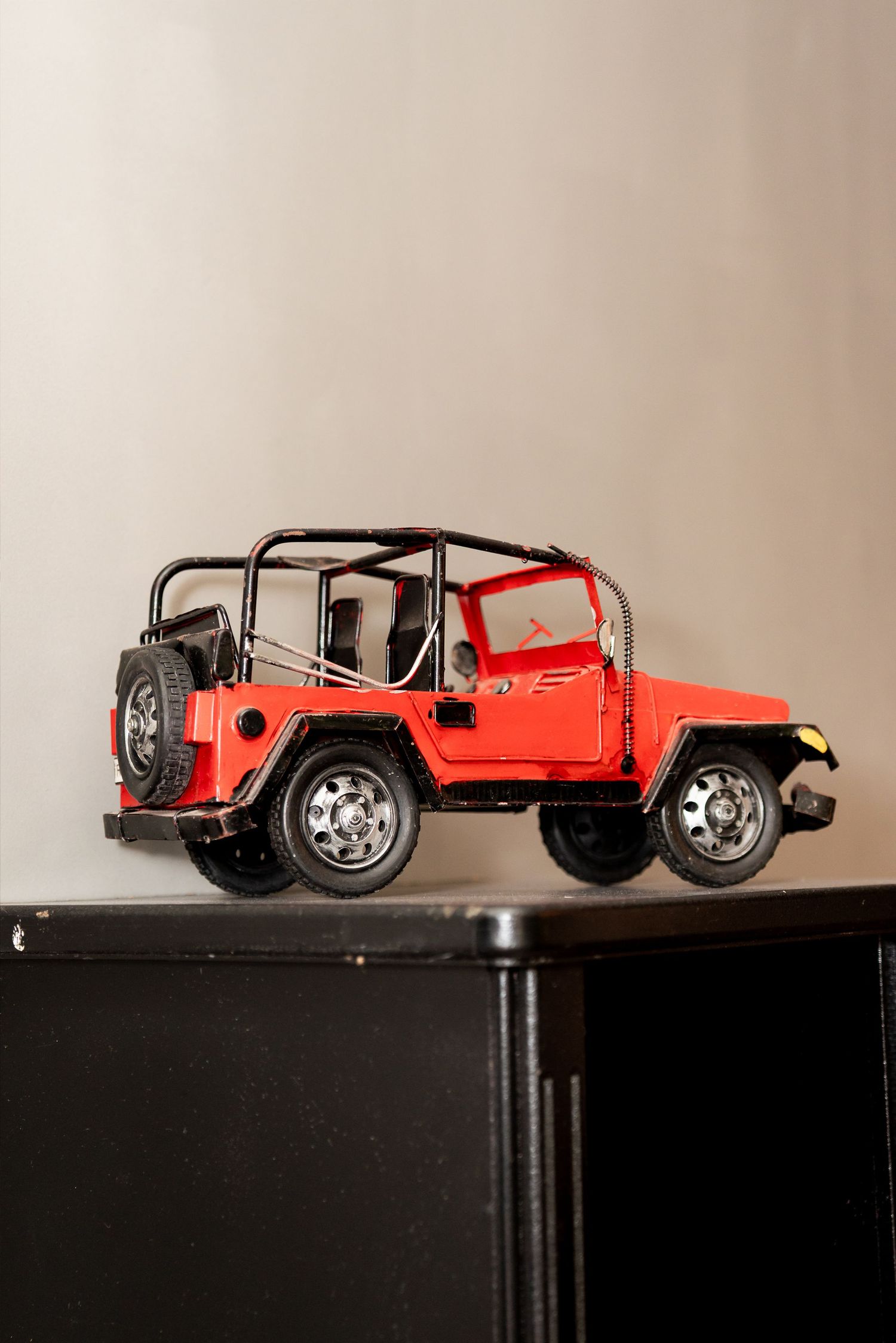 Red metal Jeep Wrangler toy model displayed on a black cabinet against a neutral wall.