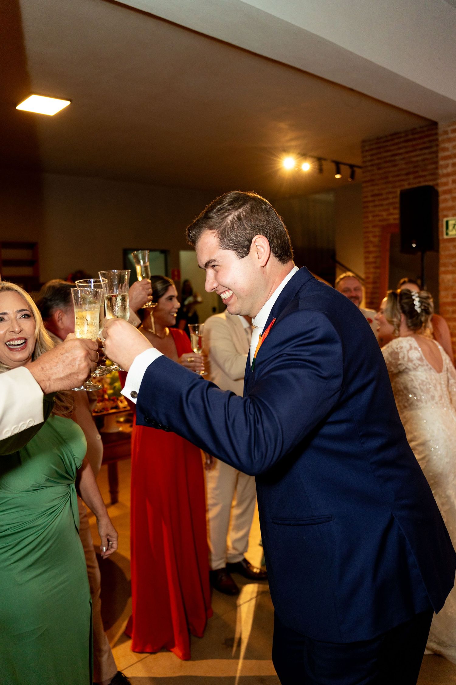 Guests toasting with champagne glasses at a wedding reception, man in navy suit smiling.