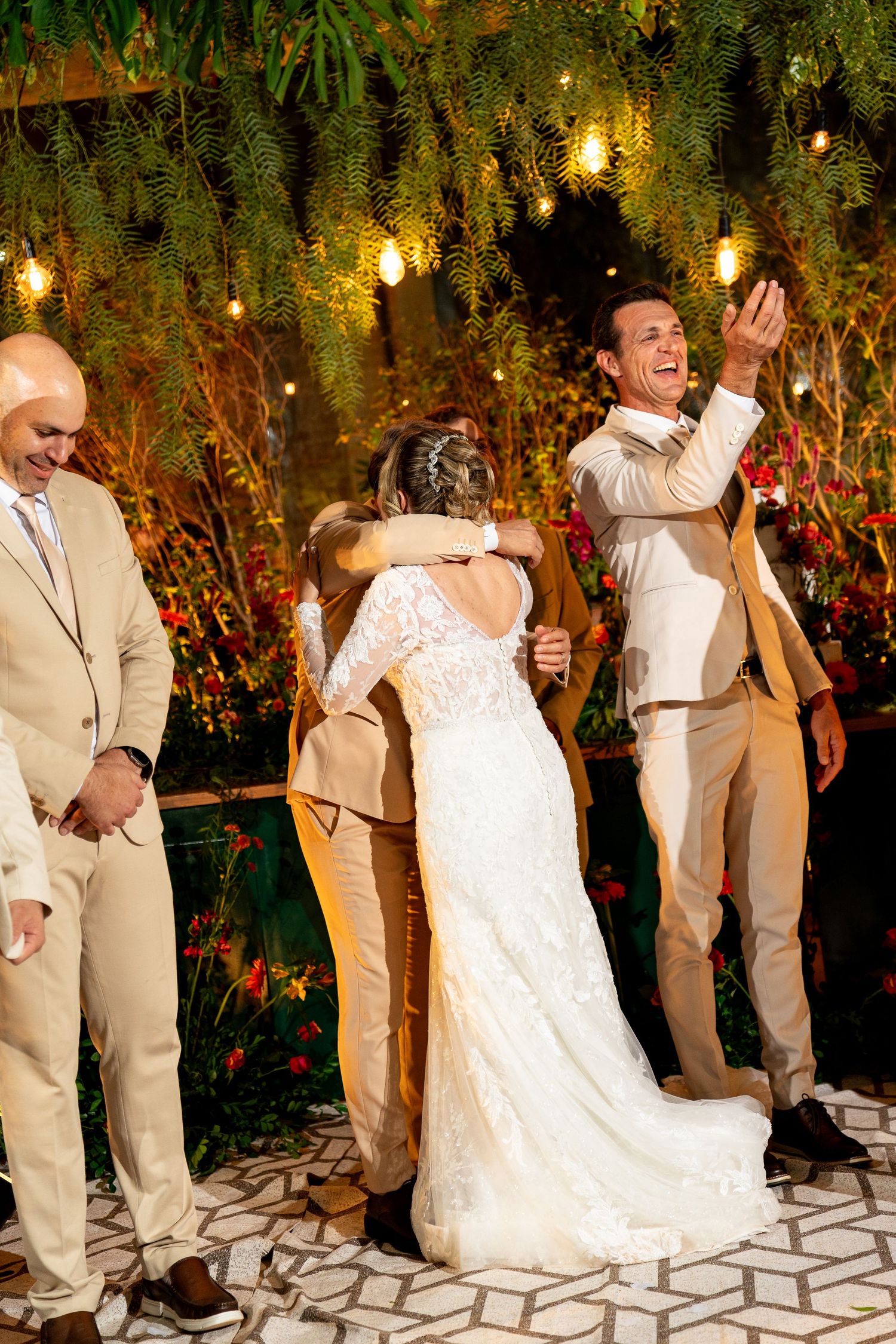 Bride and groom celebrate joyfully at outdoor wedding ceremony with warm string lights and tropical floral decor.