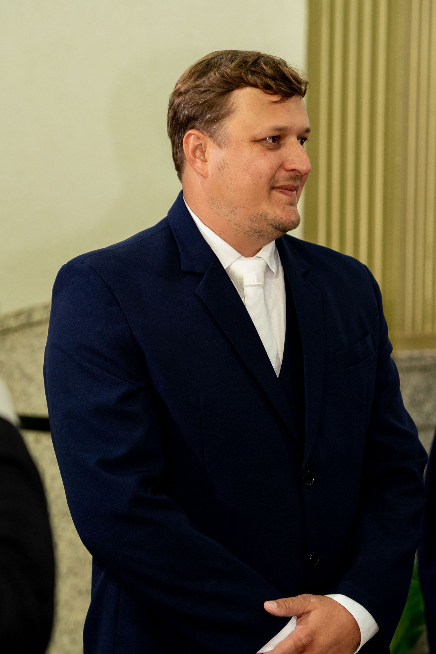 A man in a navy blue suit and white dress shirt smiling at a formal event.
