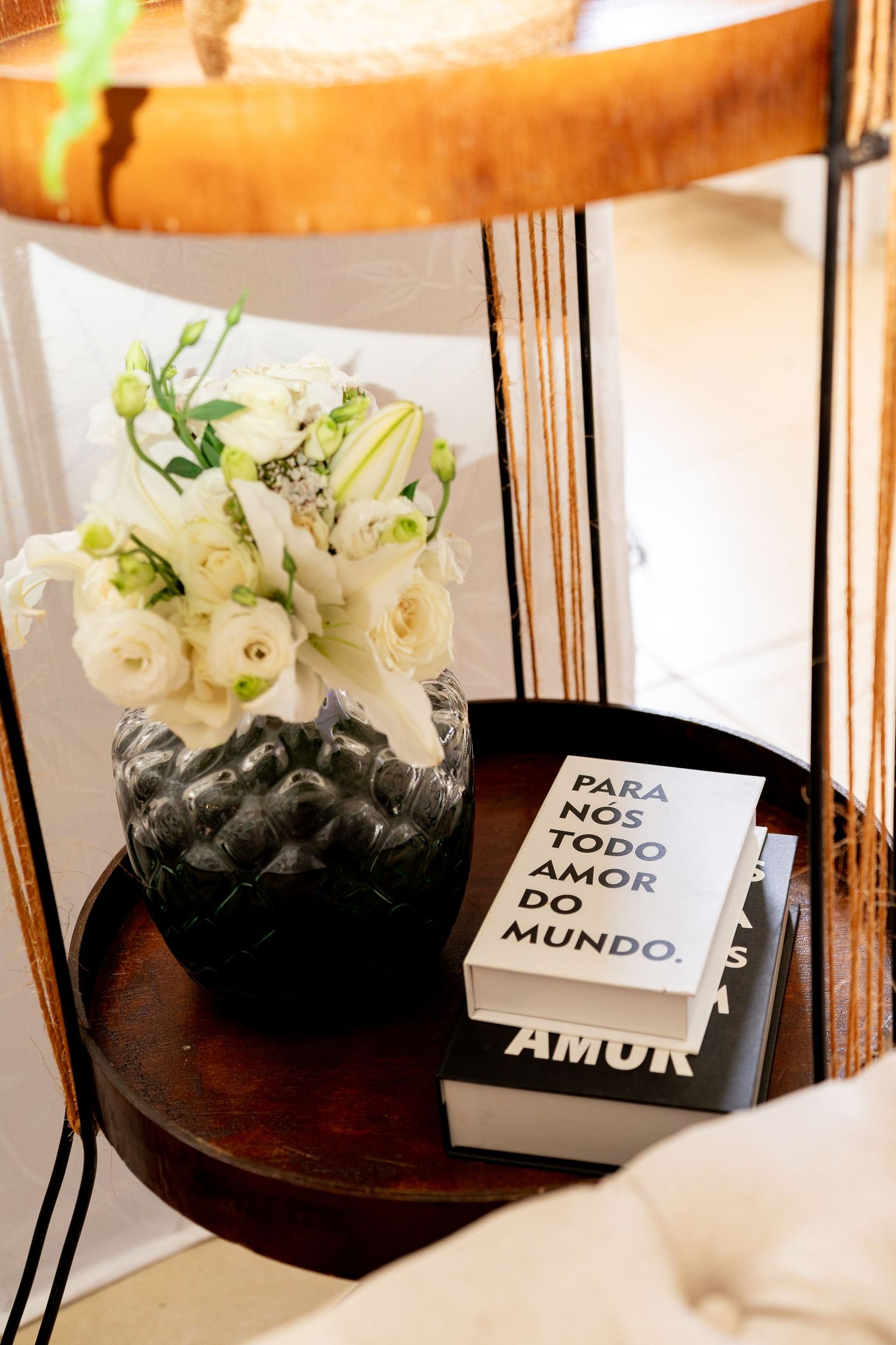 A dark vase with white flowers beside books reading Para Nos Todo Amor Do Mundo on a wooden table.