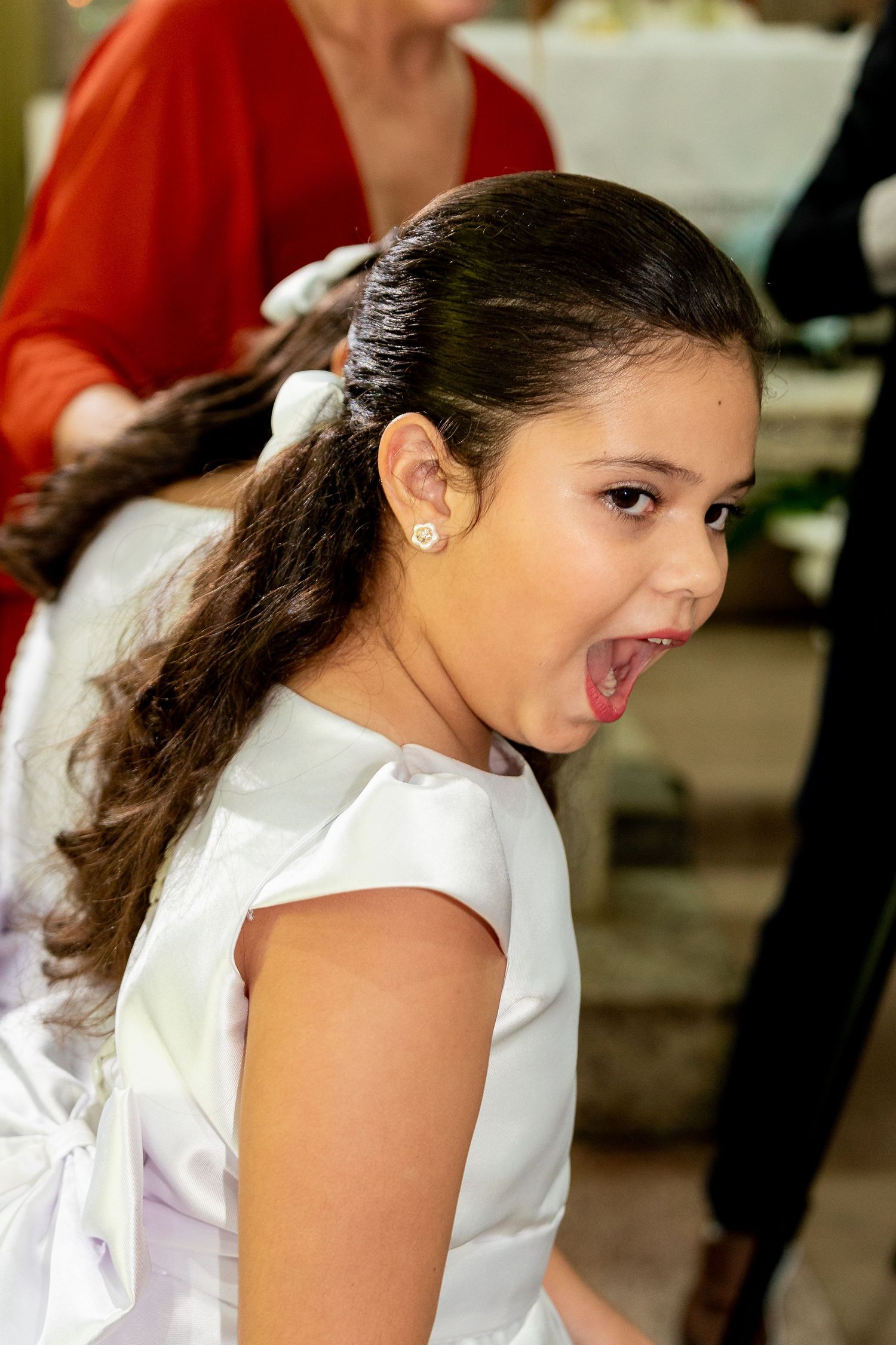 Young girl in white dress with pearl earring smiling at a formal event, dark hair in ponytail.