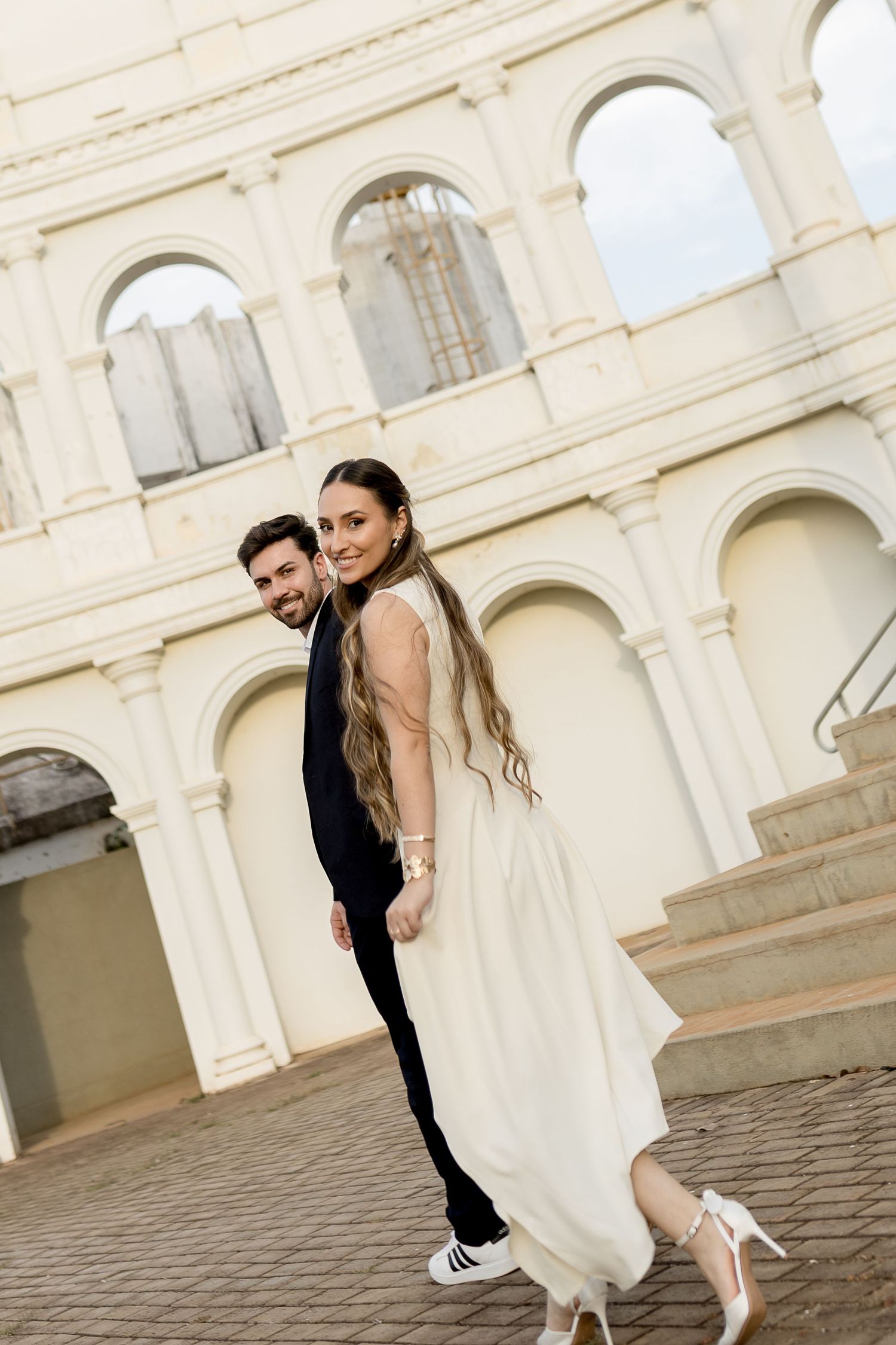 Bride in white gown and groom in black suit pose romantically in front of the Colosseum in Rome.