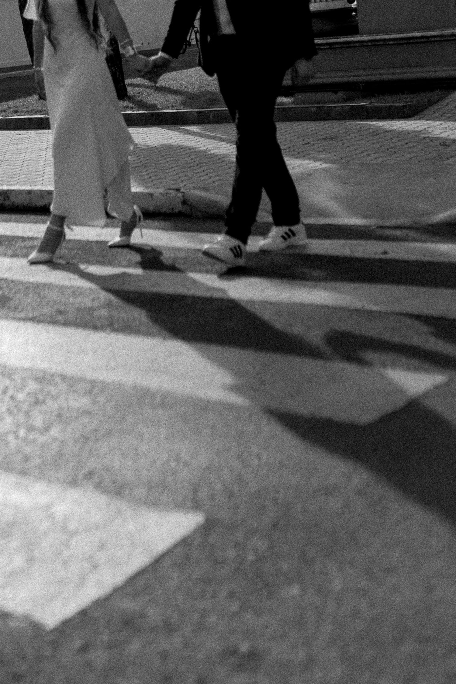 Black and white photo of two people crossing a zebra crossing, casting dramatic shadows on the pavement.
