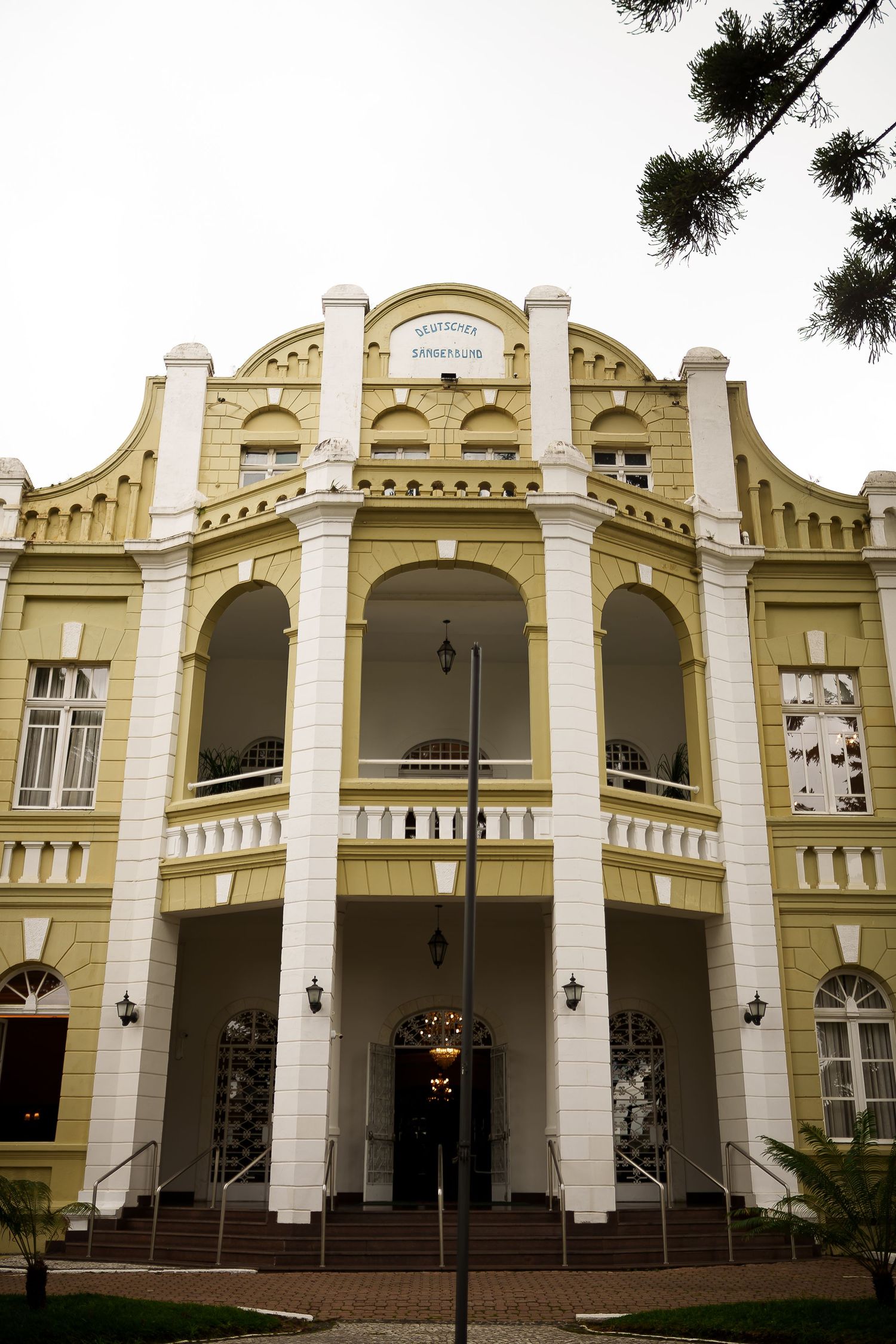Grand yellow colonial building with white columns, arched windows, and ornate facade, featuring a central balcony and entrance steps.