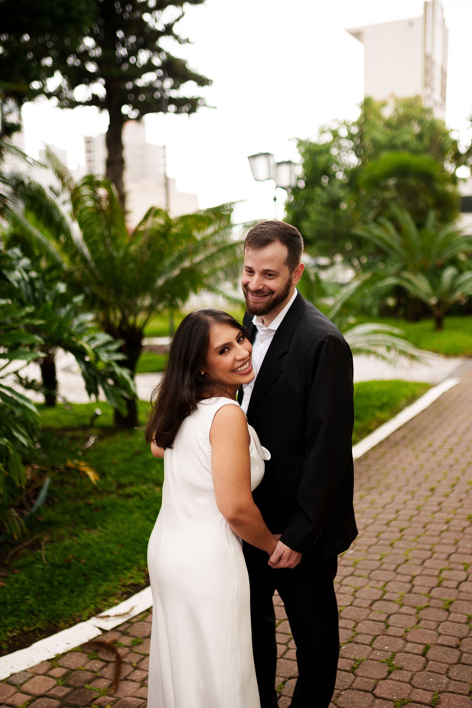 Couple in wedding attire embracing on a garden pathway surrounded by lush tropical greenery.