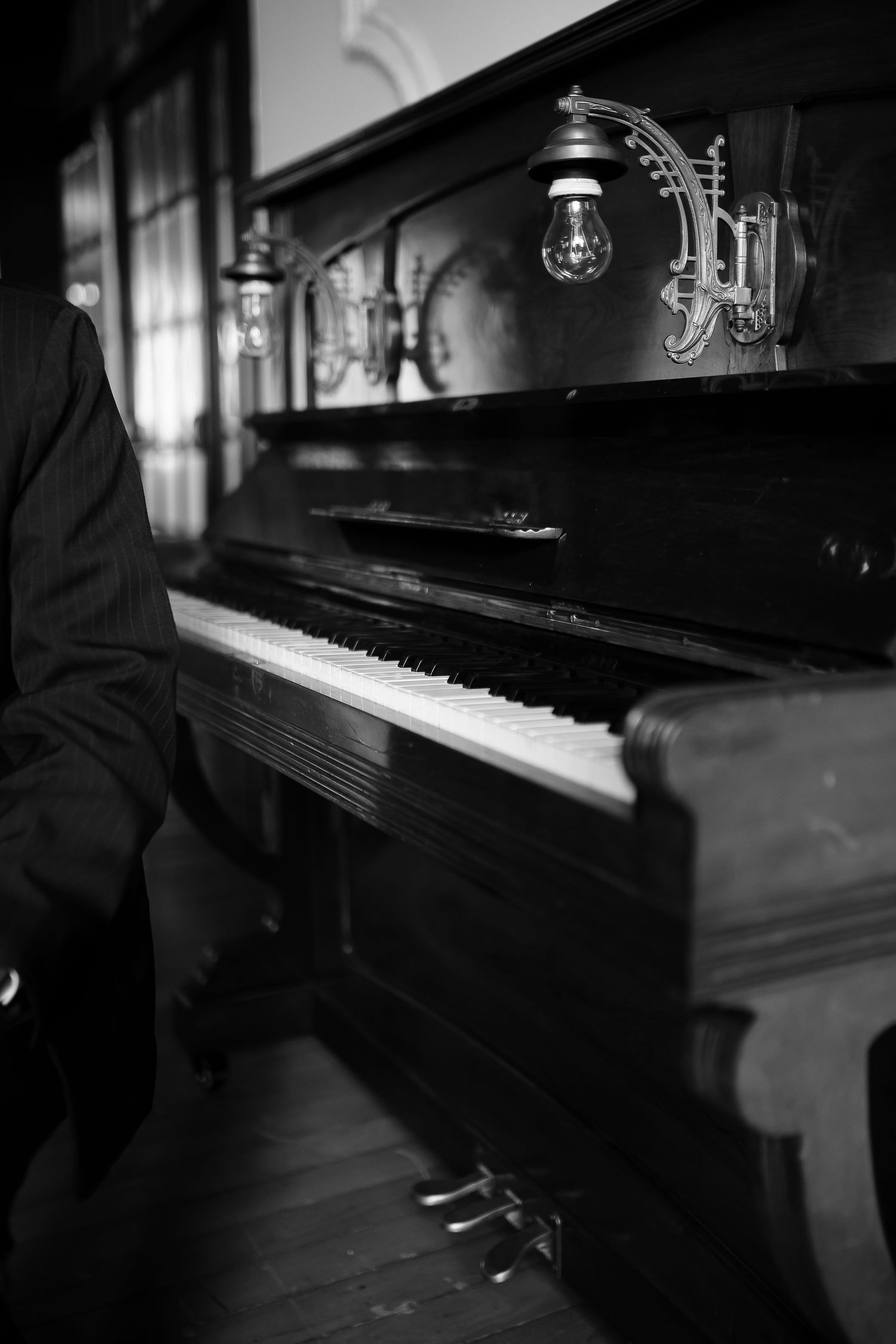 Black and white photo of a pianist playing an antique upright piano with ornate brass candle holders.