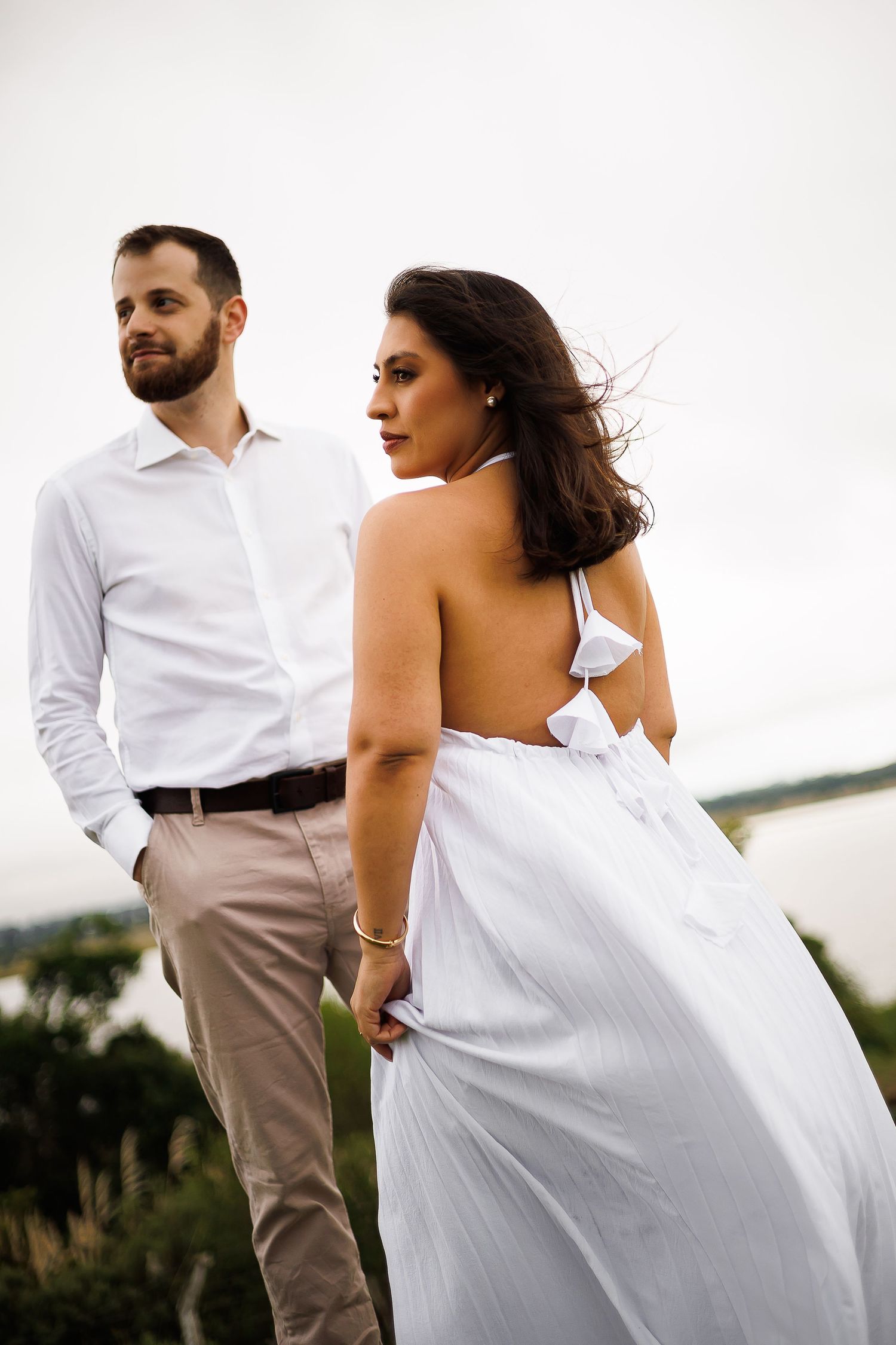 Couple in white outfits outdoors, woman in backless halter dress, man in white shirt and khaki pants.