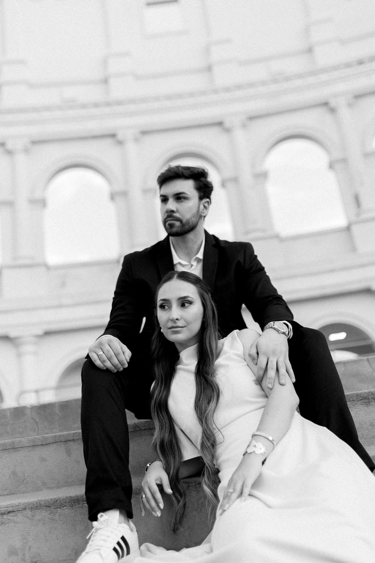 Black and white photo of an elegant couple sitting on steps in front of the Colosseum in Rome, Italy.