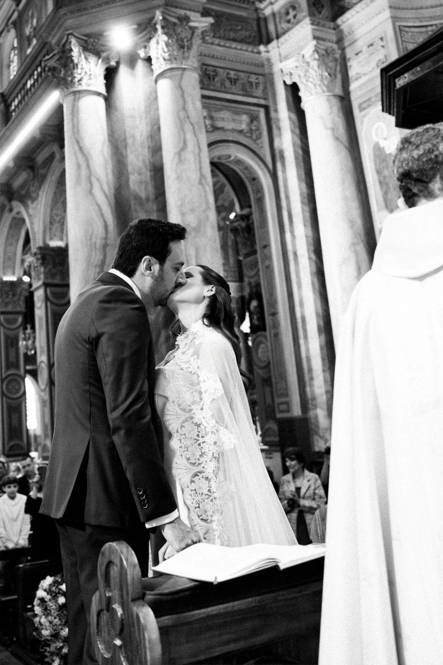 Black and white photo of a bride and groom sharing their first kiss at the altar during a church wedding ceremony.