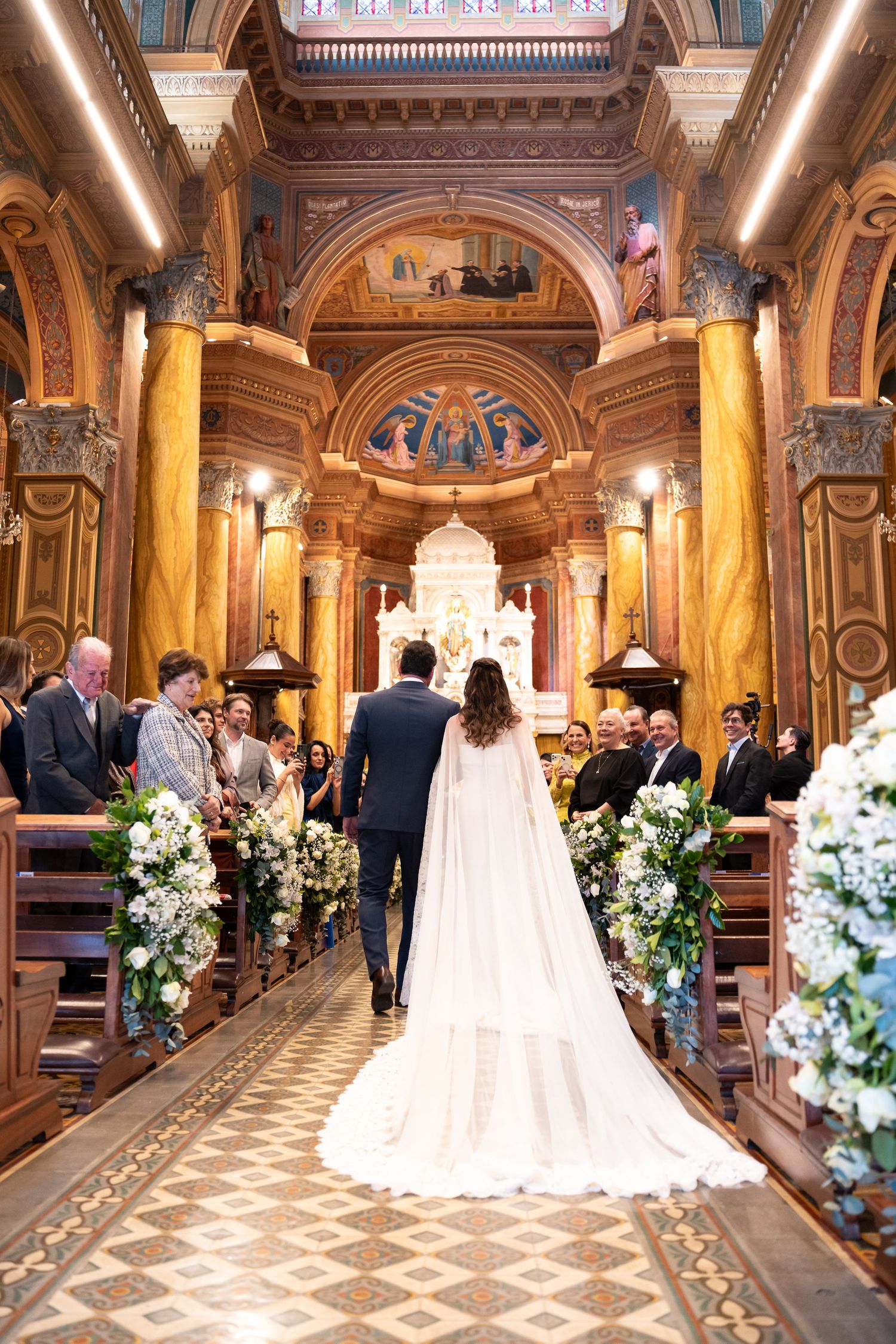 Bride and groom walking down the aisle of an ornate church adorned with floral arrangements during a wedding ceremony.