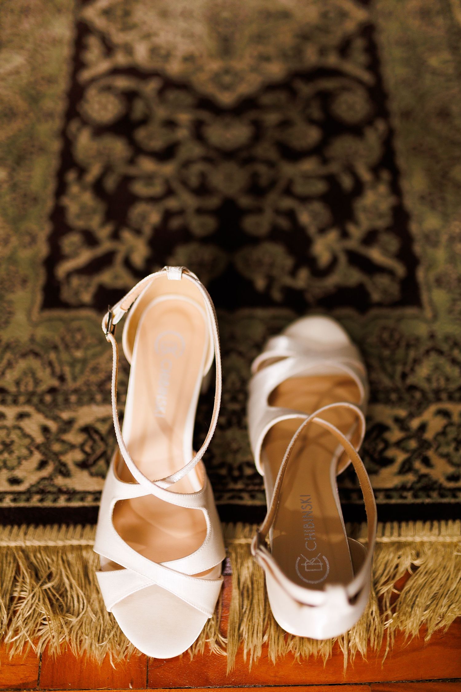 Elegant white strappy bridal heels displayed on a vintage ornate rug, perfect for a wedding day.