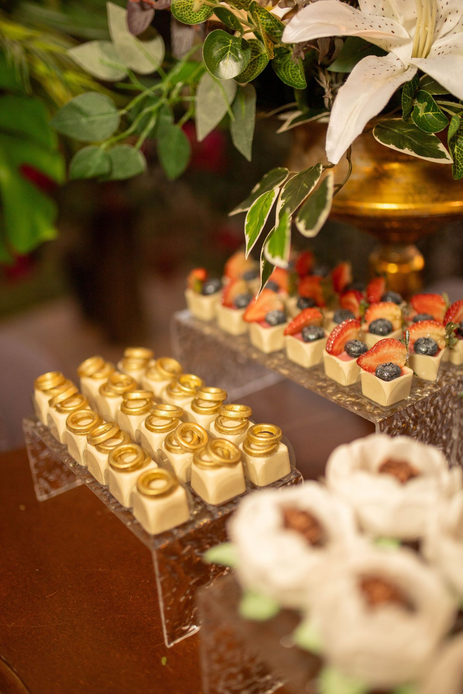 Elegant dessert display with gold-topped petit fours and fresh berry tarts on crystal stands at a luxury event.