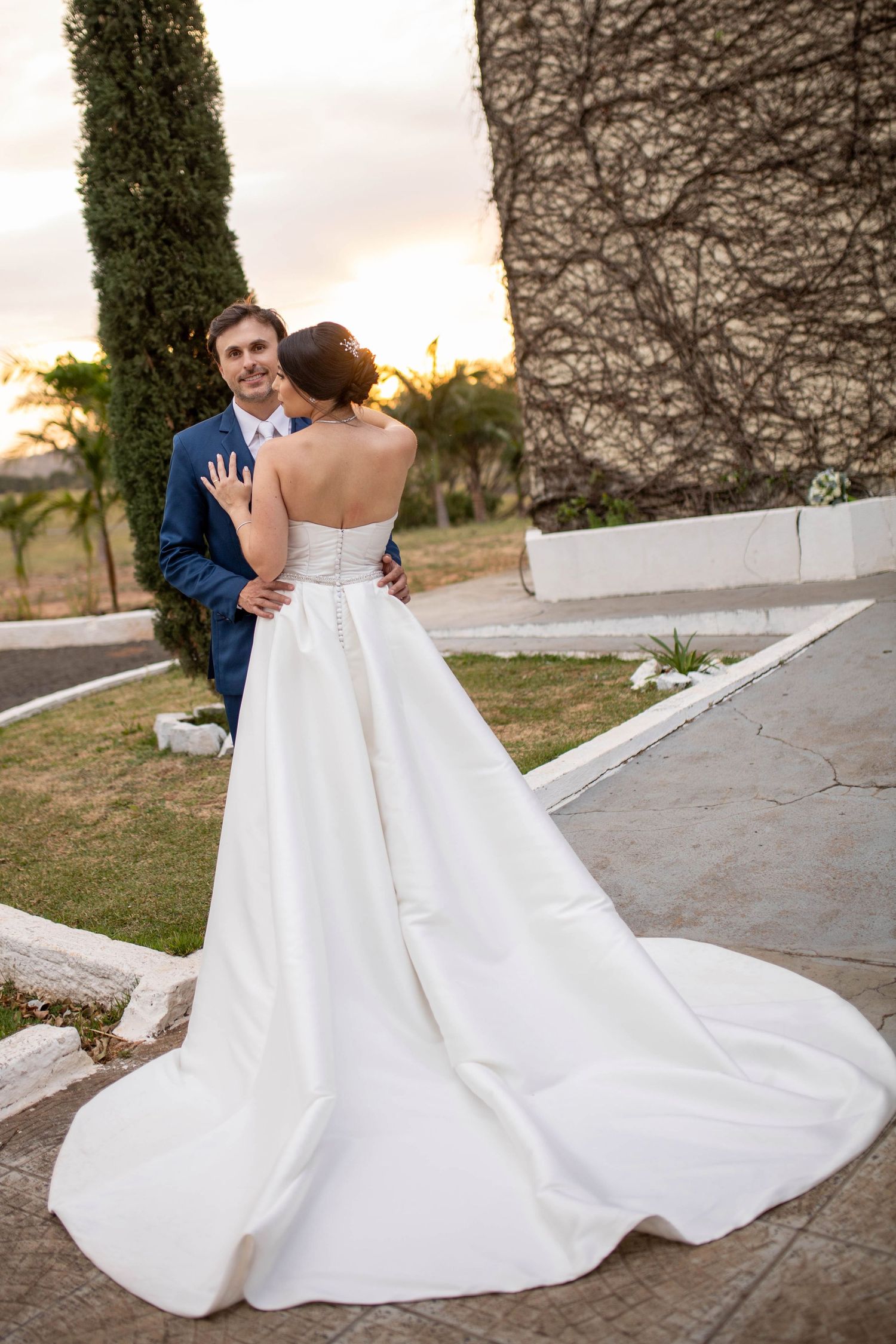 Bride and groom embracing at sunset outdoors, bride in strapless white gown with elegant long train.