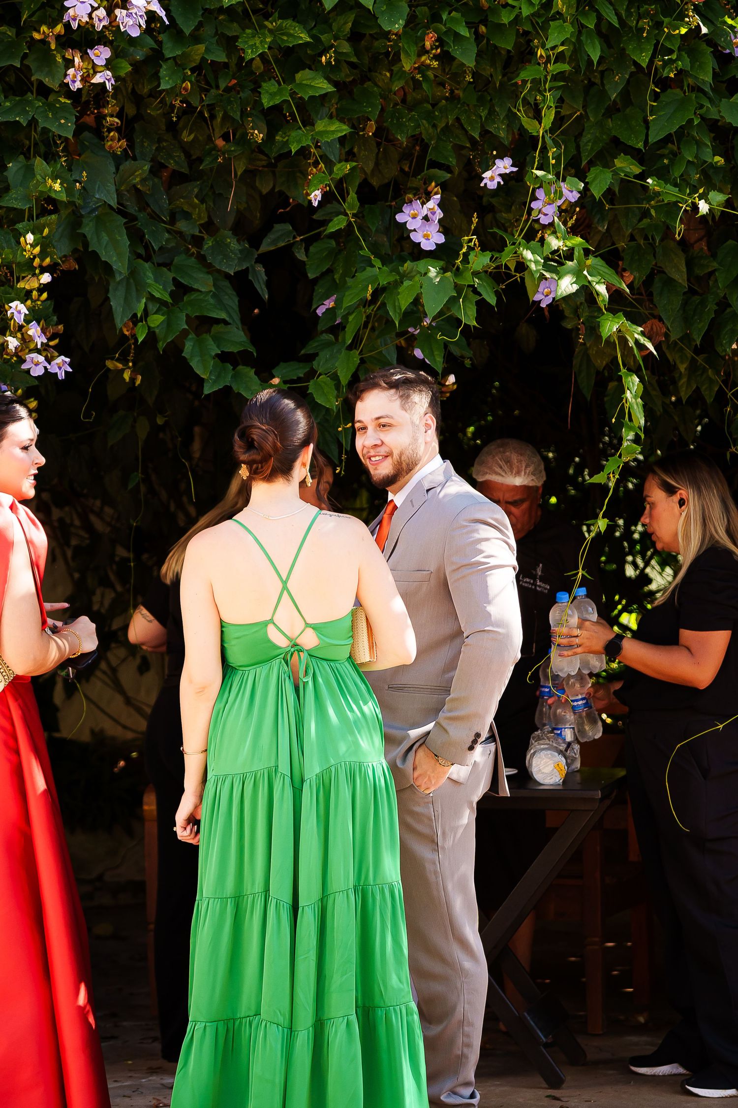 Guests in elegant attire mingle outdoors under lush greenery at a wedding reception.