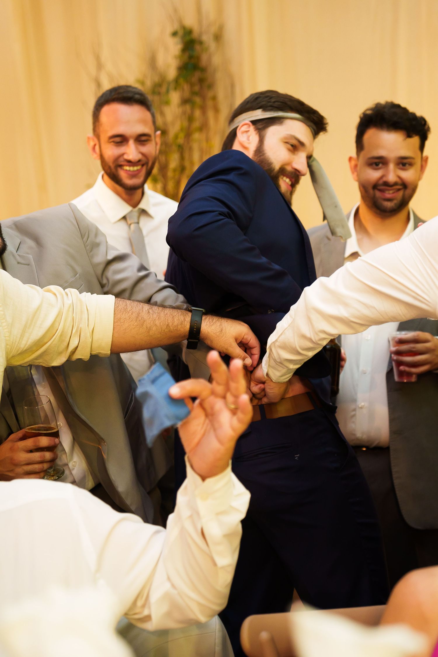 Group of smiling men in formal attire gathered together at a celebration, sharing a joyful moment.