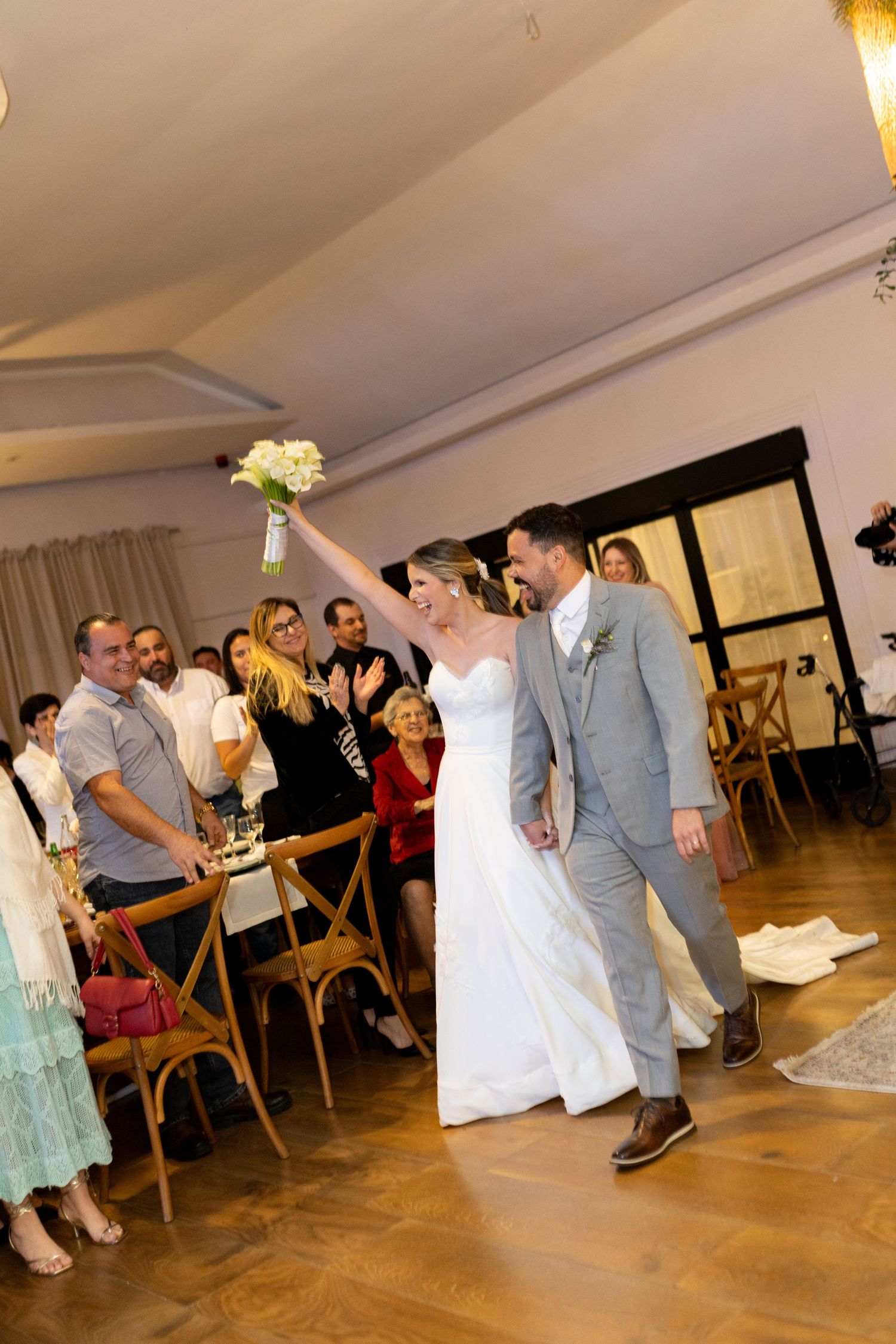 Joyful newlyweds walk down the aisle as bride raises bouquet, guests celebrating in elegant indoor wedding venue.
