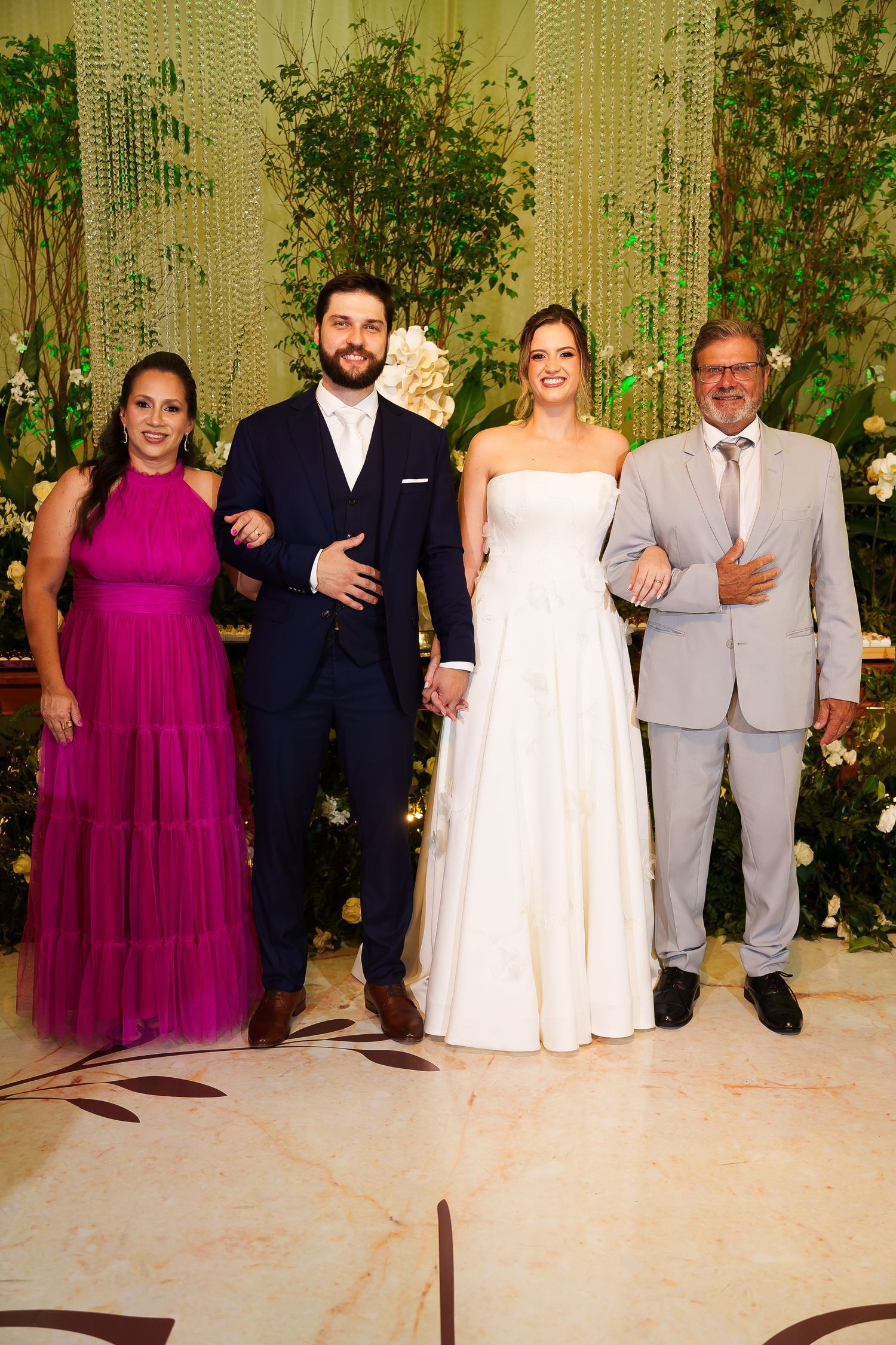 Wedding party of four posing elegantly, bride in white gown, groom in navy suit, woman in magenta dress, man in gray suit.