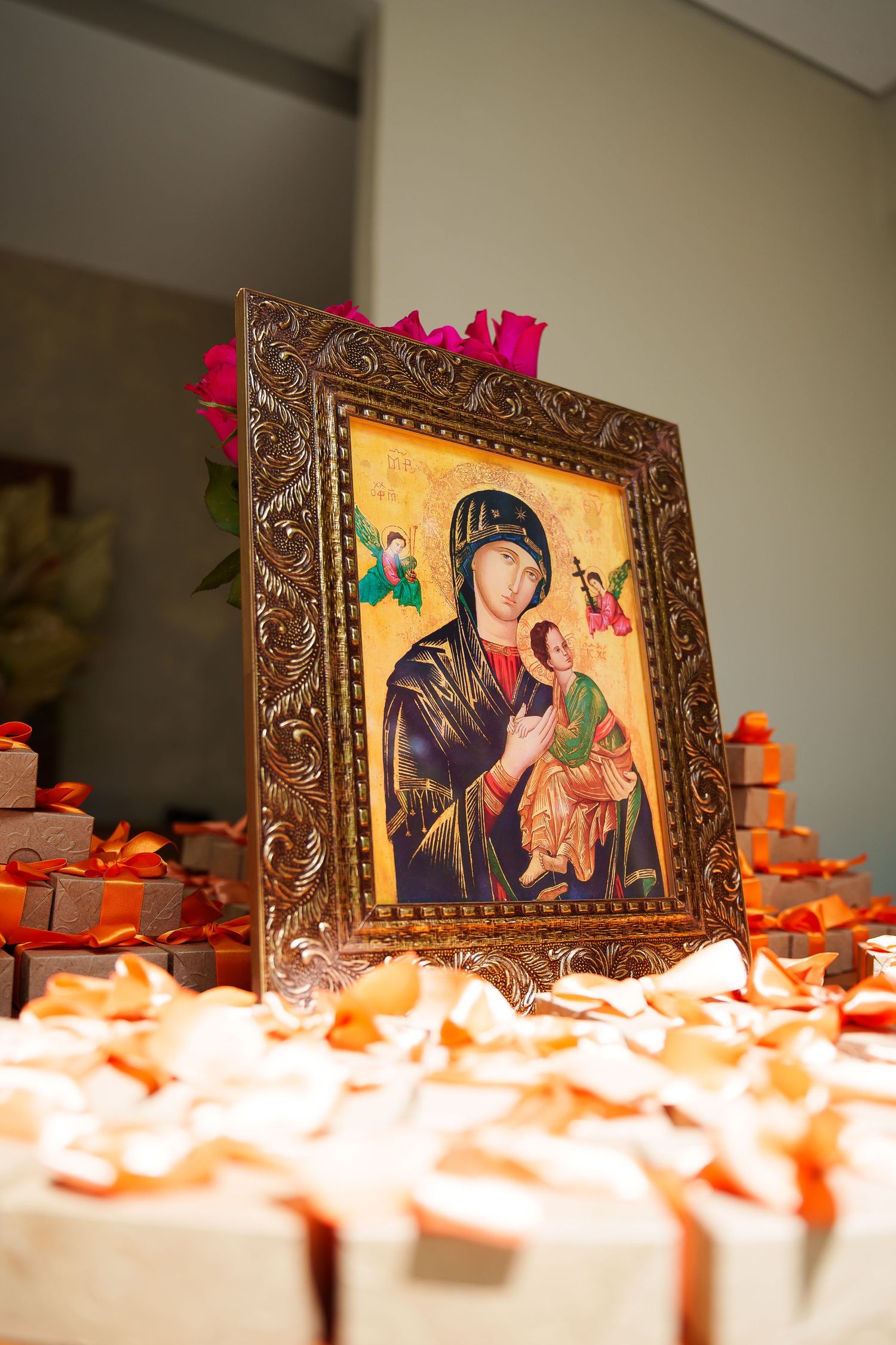 Ornate framed icon of Our Lady of Perpetual Help surrounded by gift boxes with orange ribbons and rose petals.