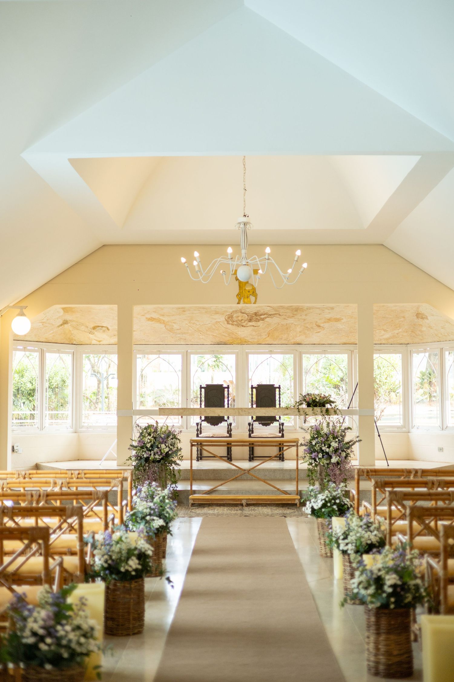 Elegant chapel wedding venue with floral arrangements lining the aisle, wooden pews, and a chandelier overhead.