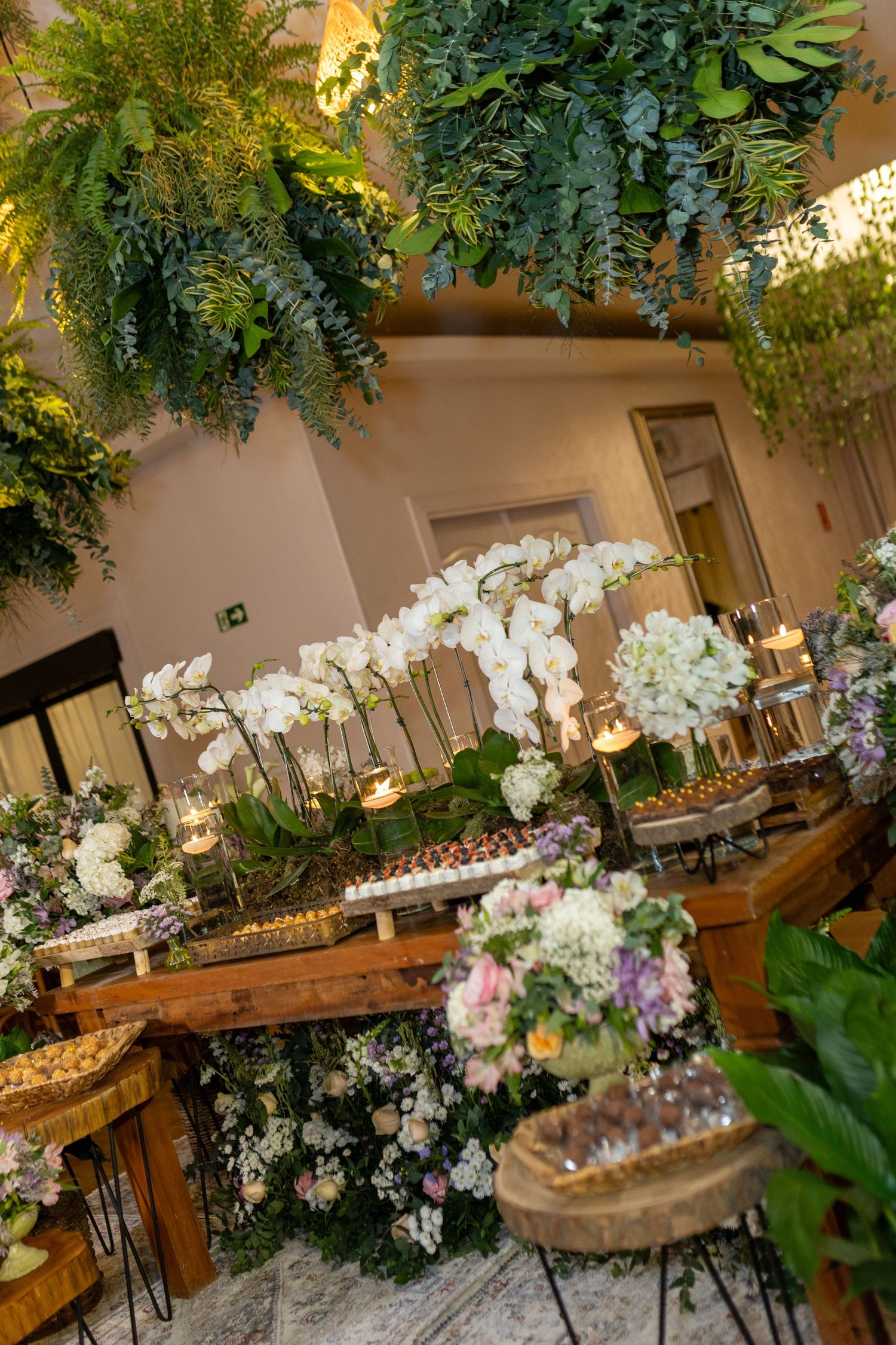 Elegant wedding reception table adorned with white orchids, candles, and lush greenery hanging overhead.