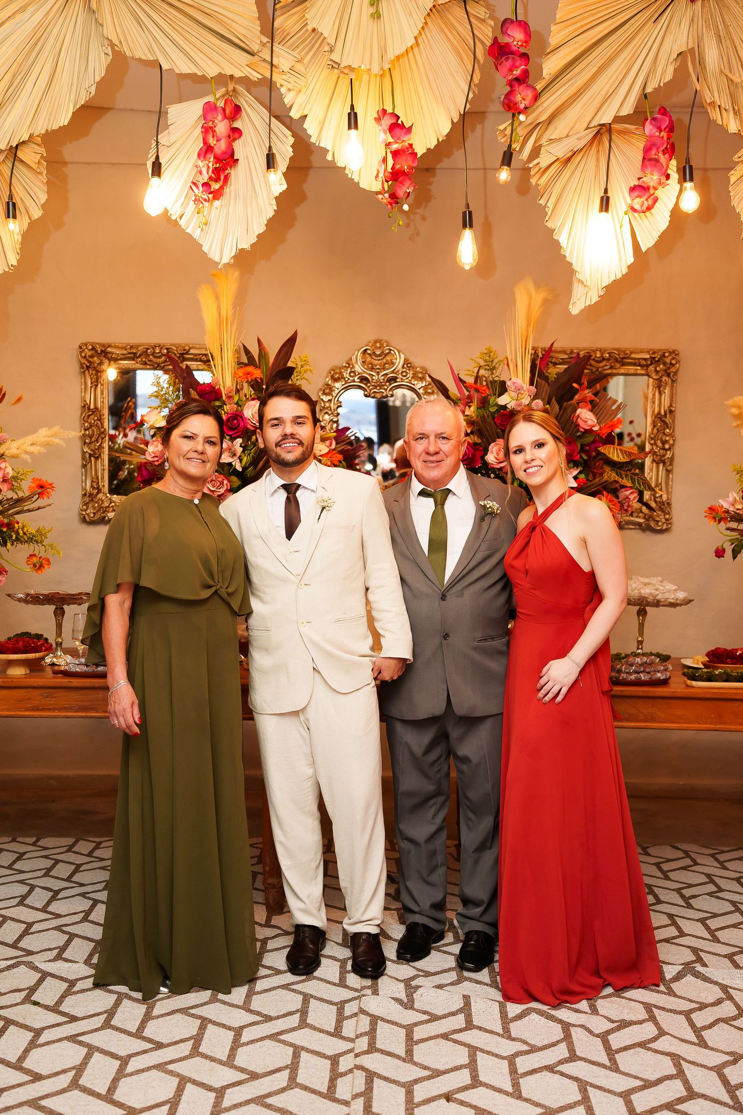 Four elegantly dressed people posing together at a wedding reception with floral decorations and warm lighting.