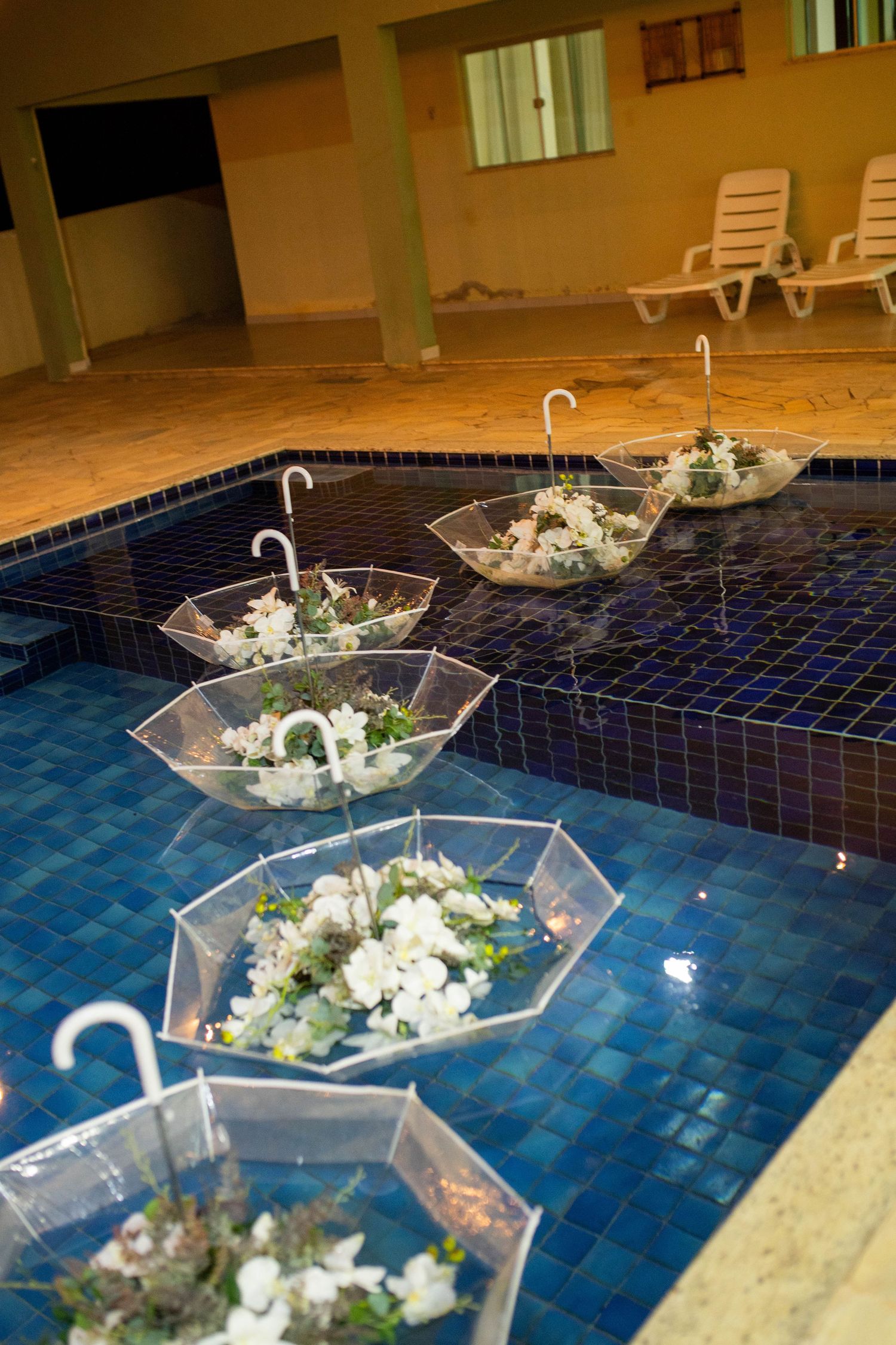 Clear umbrellas filled with white flowers floating in a blue tiled pool, creating elegant floral decorations.