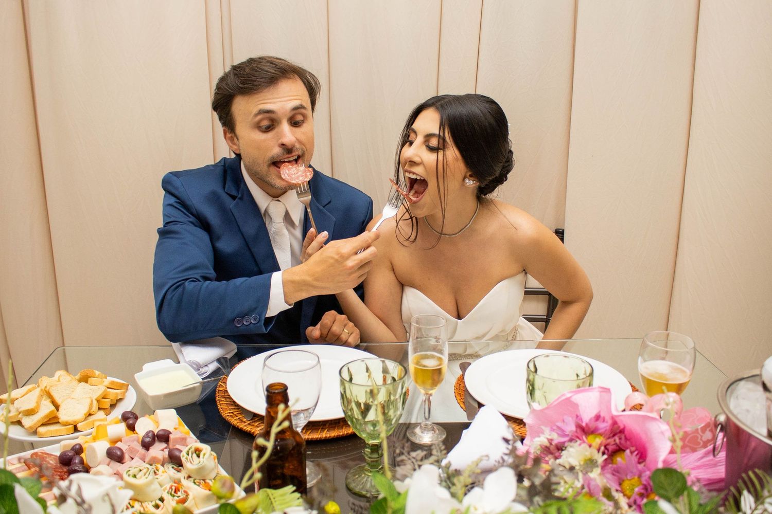 Joyful bride and groom sharing a playful moment tasting food at their elegant wedding reception table.