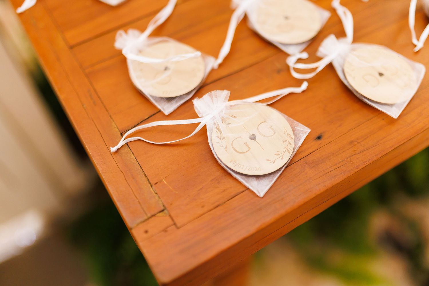 White organza wedding favor bags with ribbon ties displayed on a wooden table at a wedding reception.