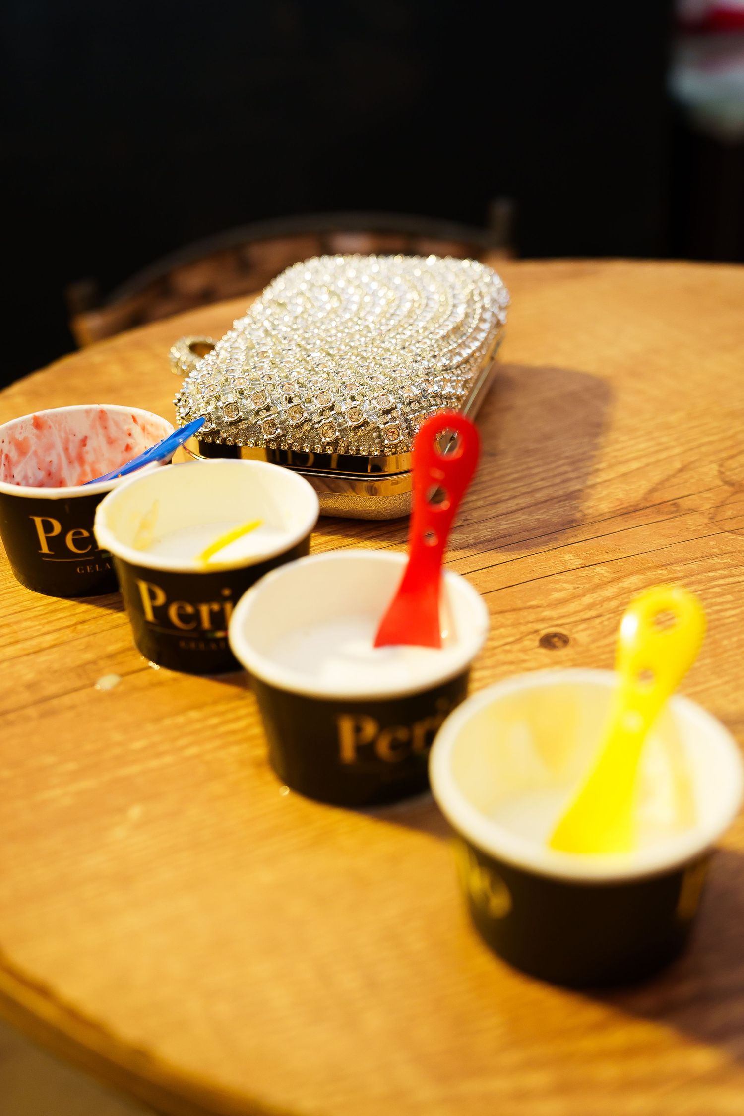 Empty ice cream cups with colorful spoons on a wooden table beside a sparkling rhinestone clutch purse.