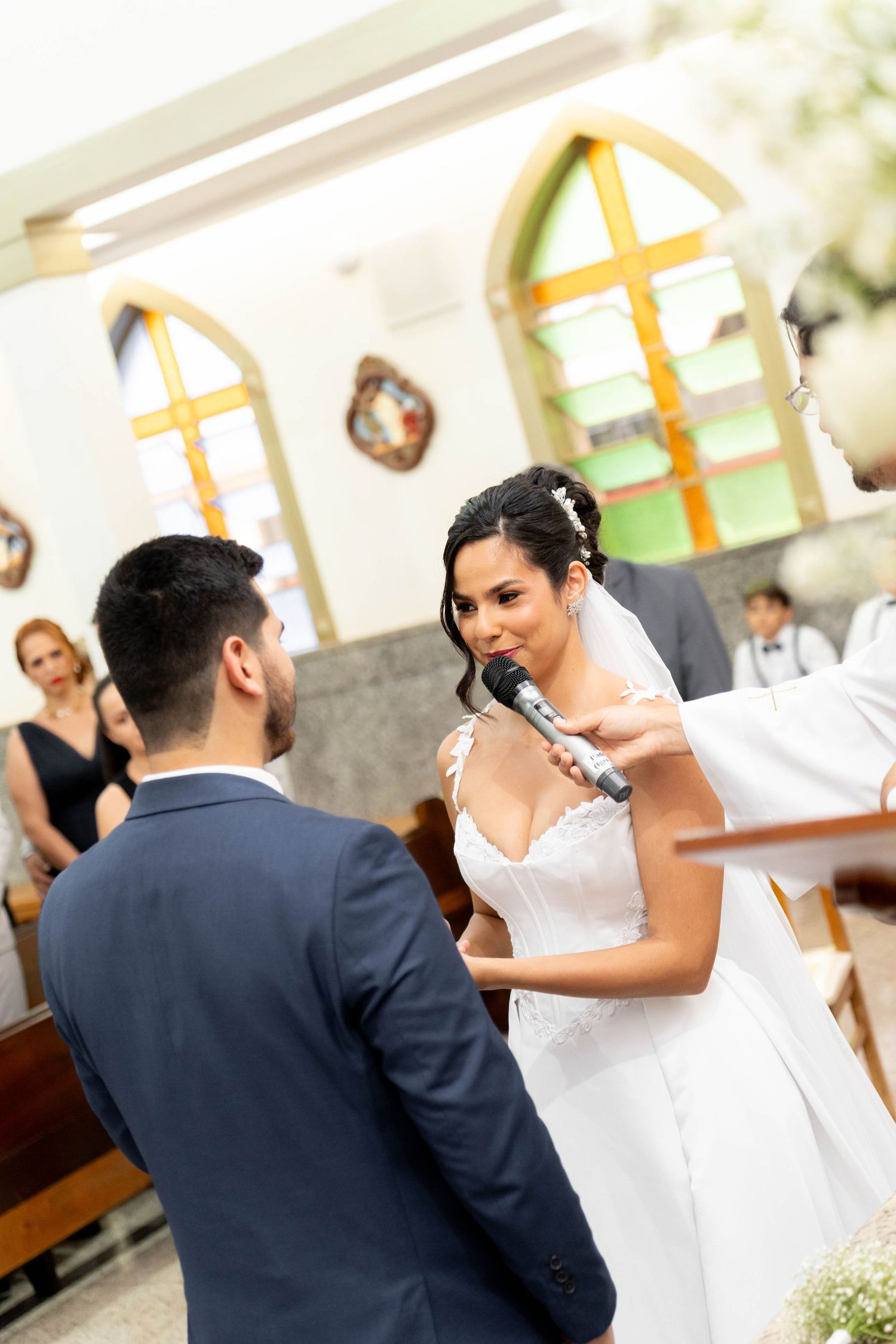 Bride in white gown recites wedding vows at church altar while groom in navy suit listens attentively.