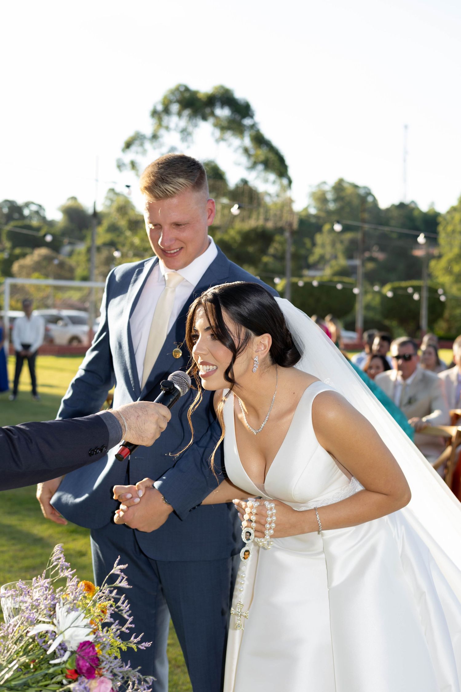 Bride and groom laughing during outdoor wedding ceremony while guest holds a small snake near the bride.